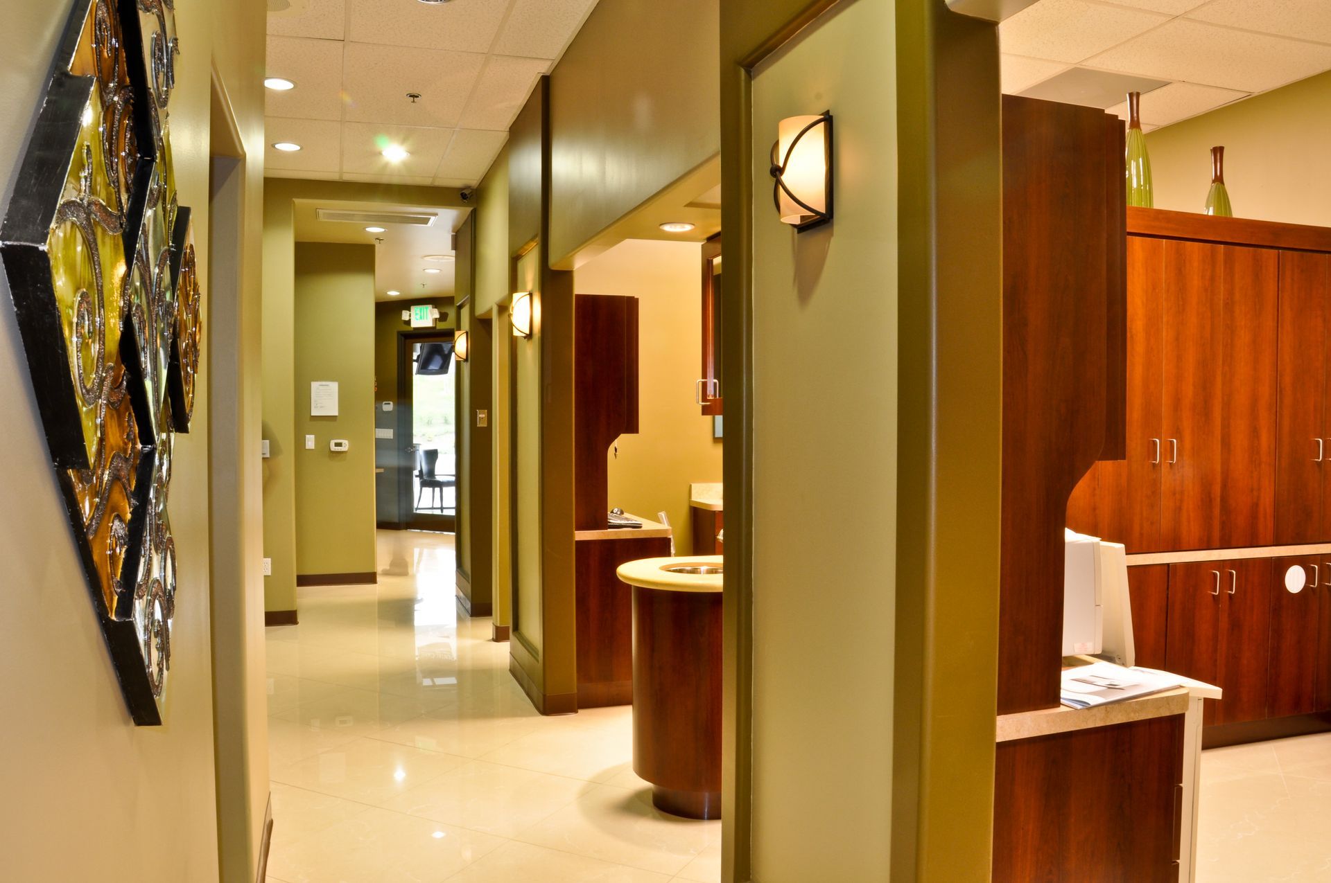 Hallway in dental office; neutral colors, wooden cabinetry, lights, door to outside.