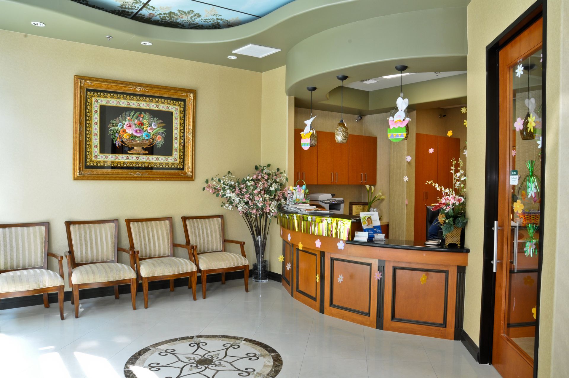 Dental office waiting room with chairs, reception desk, and floral painting.