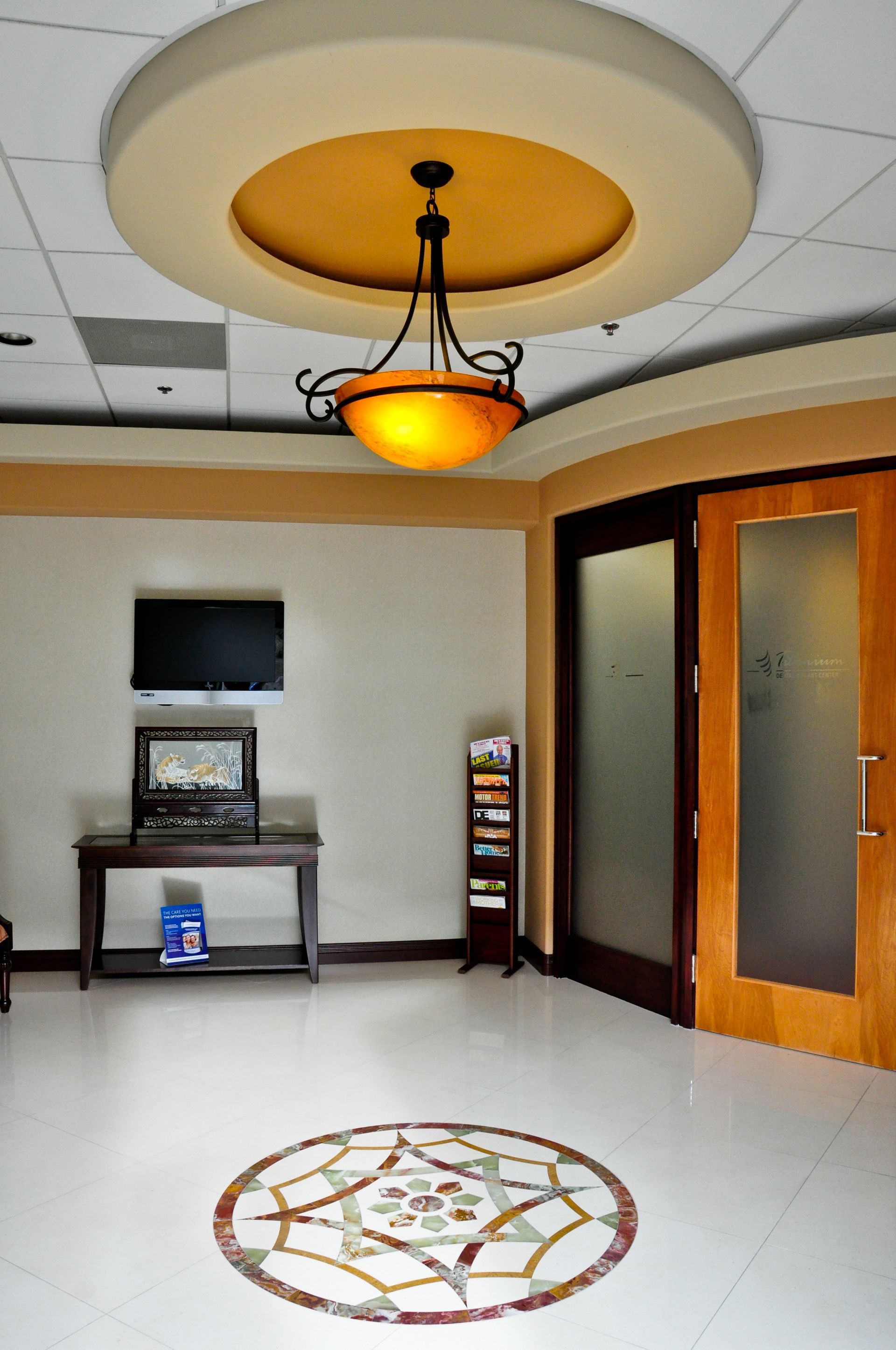 Lobby with marble floor inlay, wood trim, a dark table with TV, and a decorative light fixture.