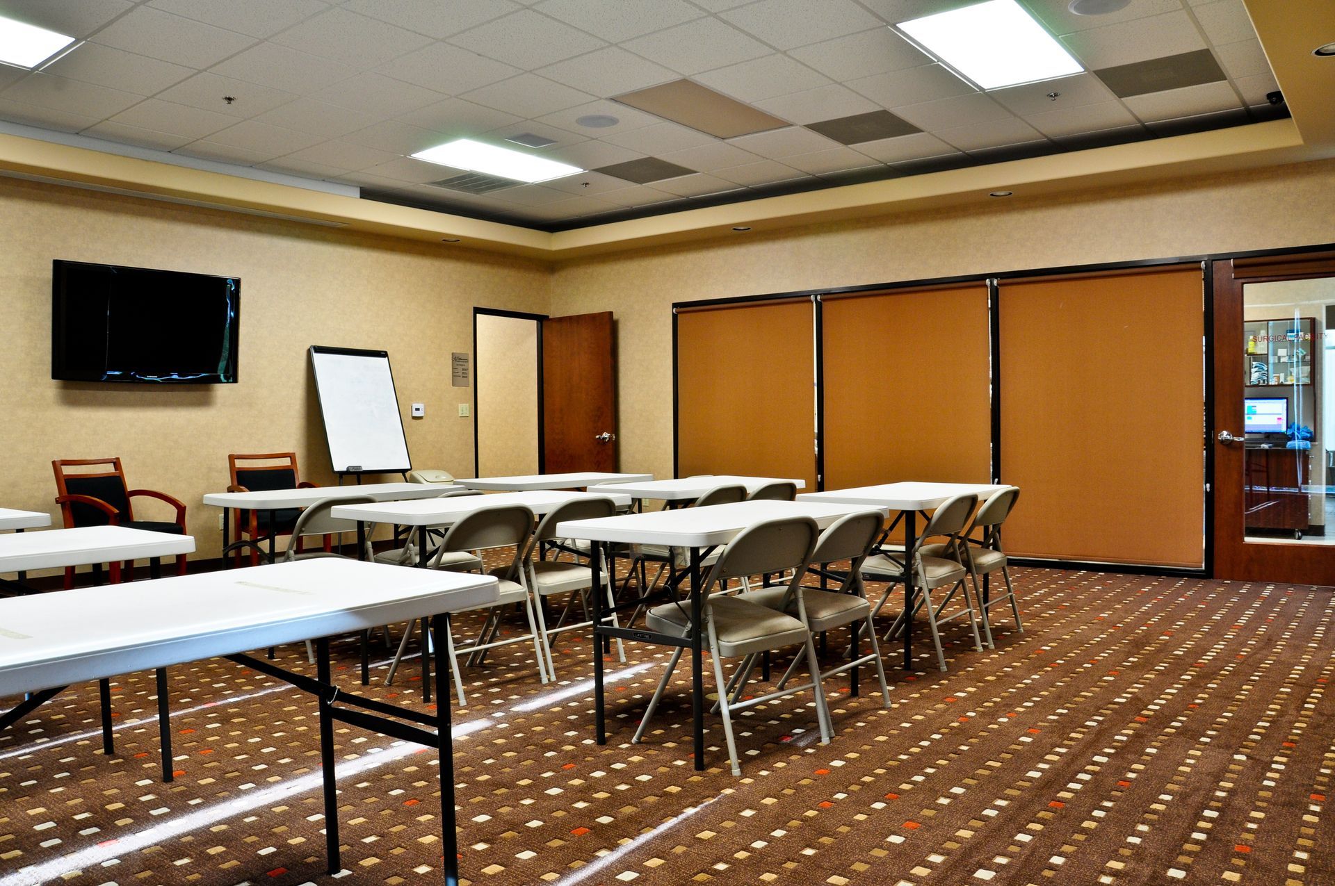 Meeting room with tables, chairs, whiteboard, and a large TV.