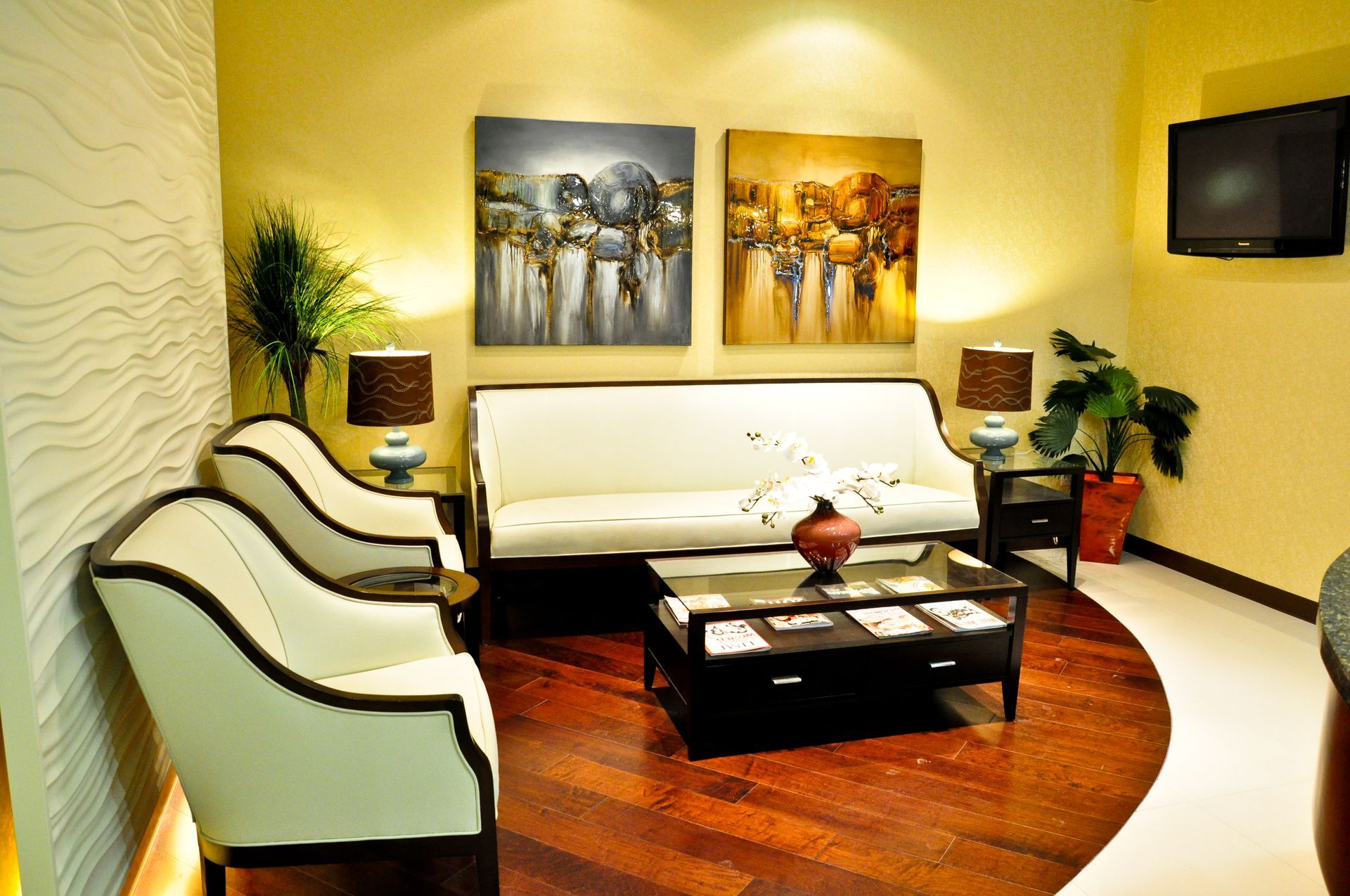 Waiting room with white seating, artwork, coffee table, and a wall-mounted TV.