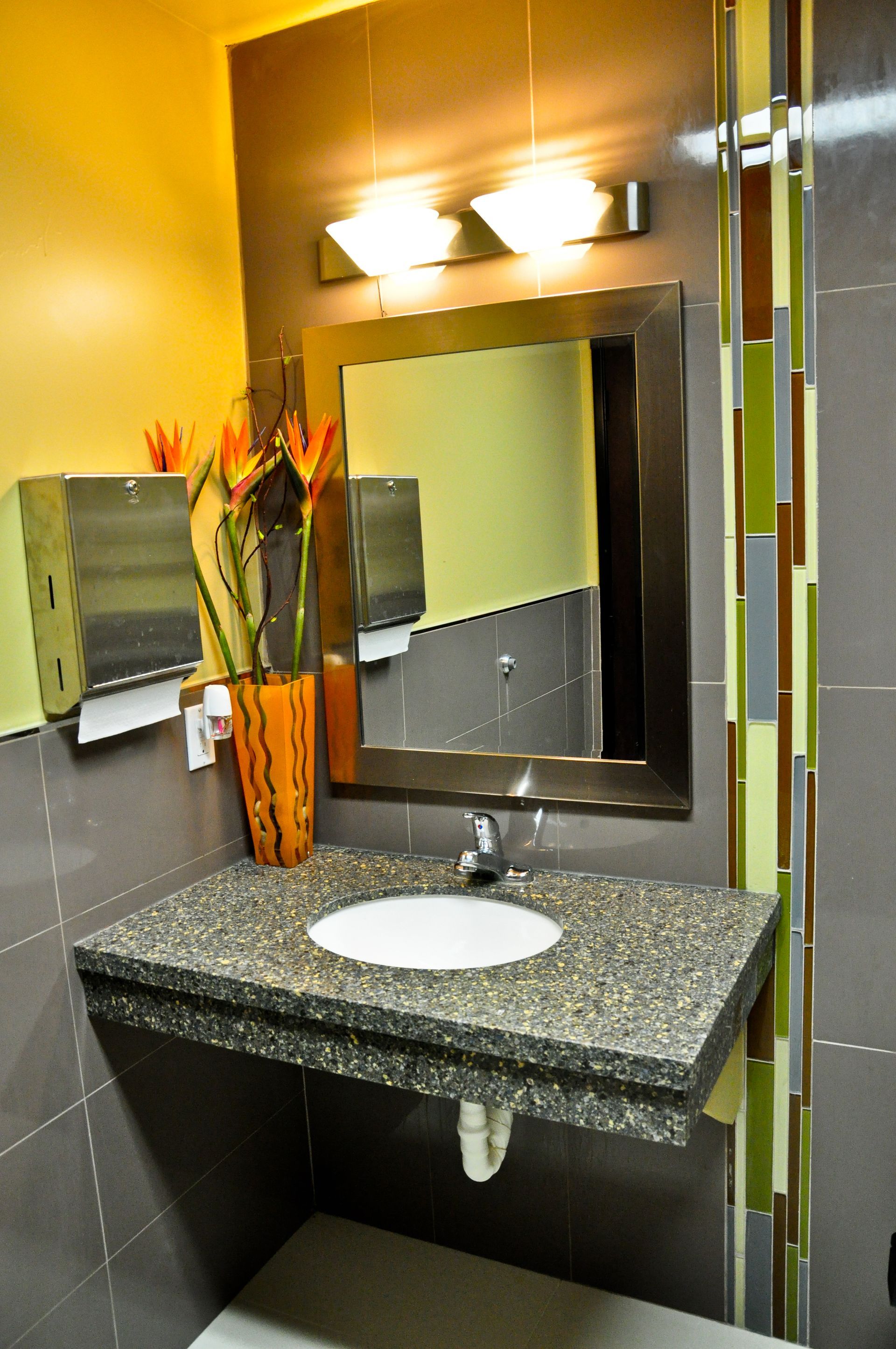 Modern public restroom with a speckled countertop sink, mirror, and flower arrangement.