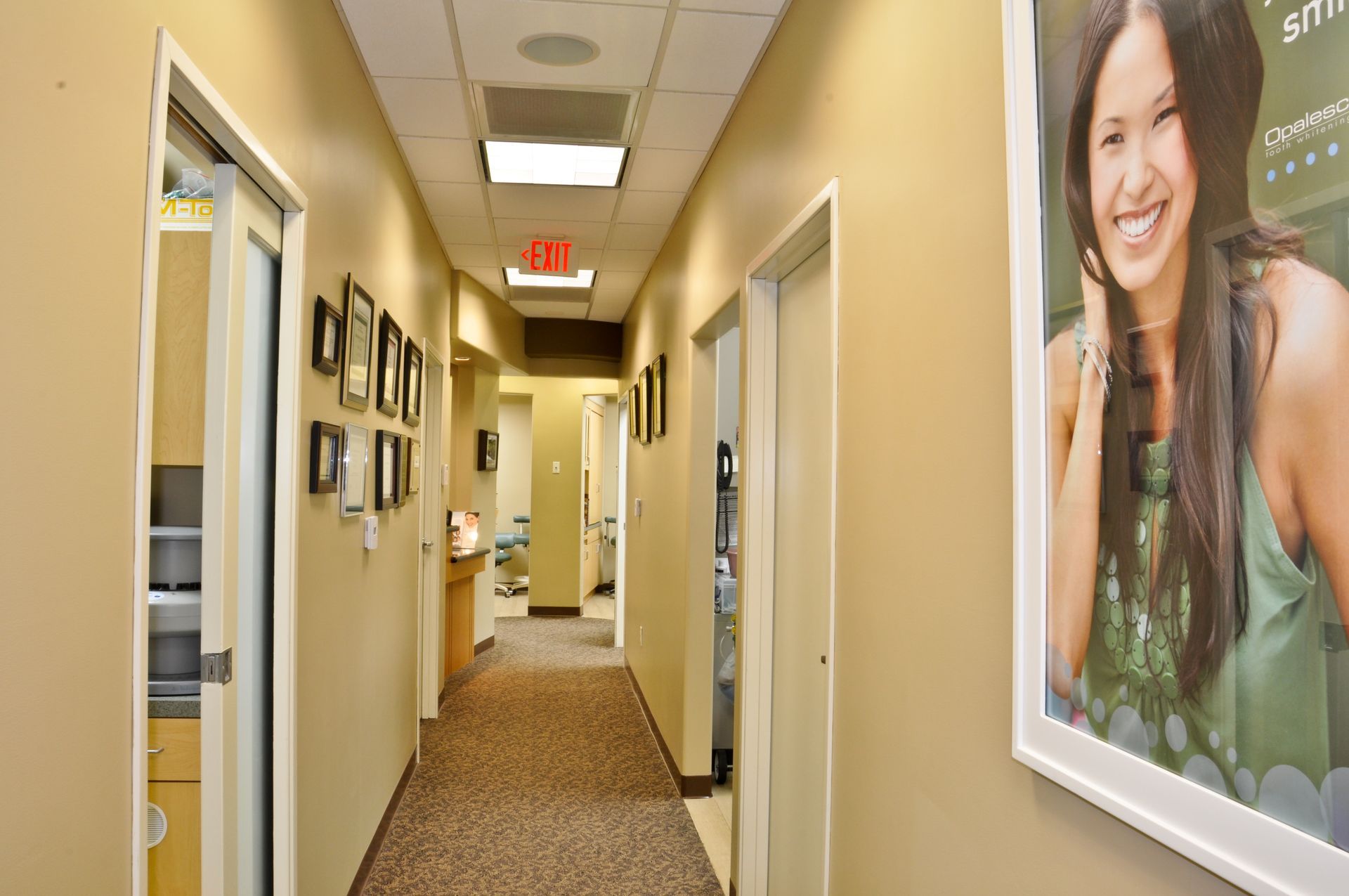 Hallway in a dental office; tan walls, brown carpet, doors on both sides, poster of woman smiling.