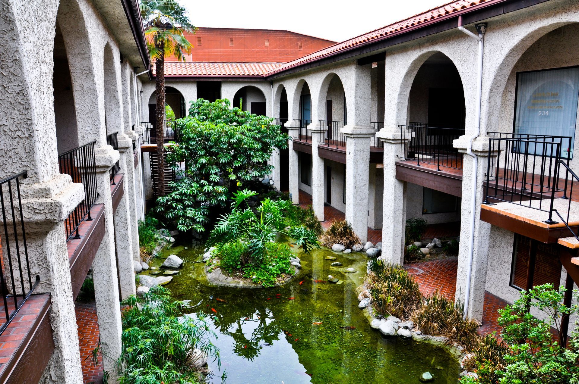 Courtyard with arched walkways overlooking a pond and lush greenery.