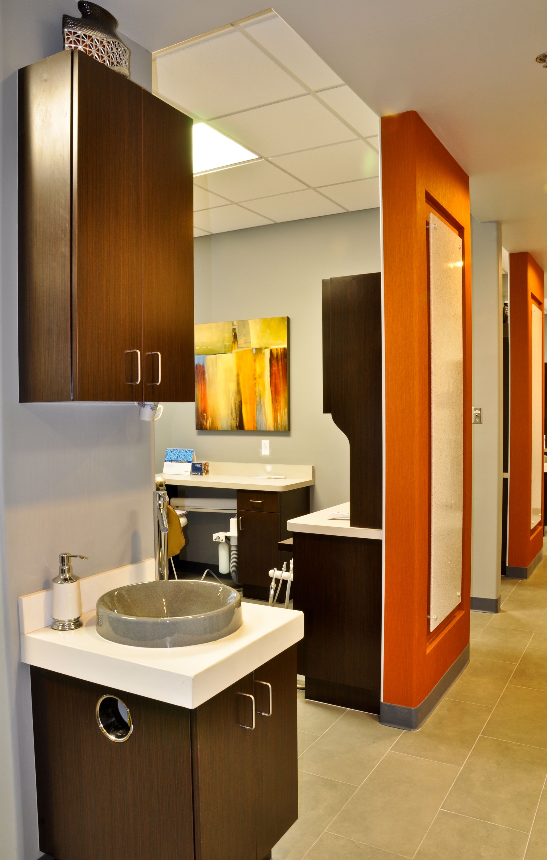 A dental office interior. Dark brown cabinets, orange accents, gray walls, and a sink.