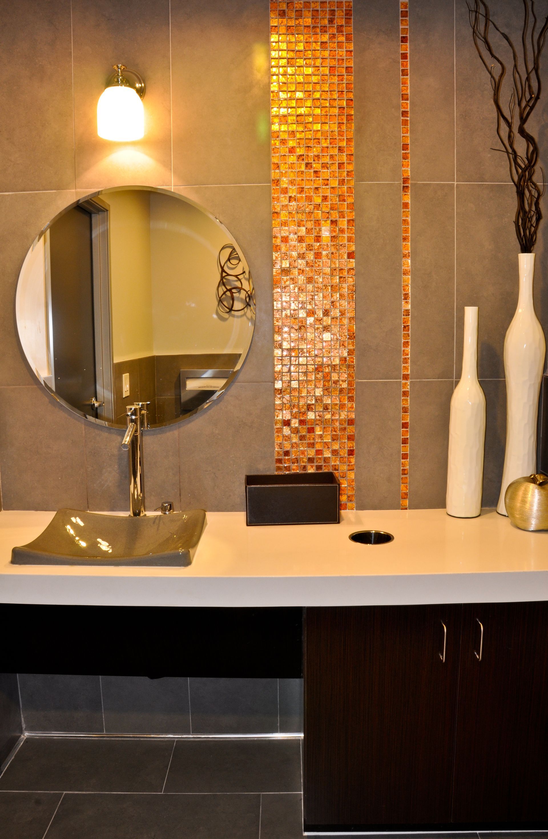 Modern bathroom with round mirror, gold sink, and orange mosaic tile.