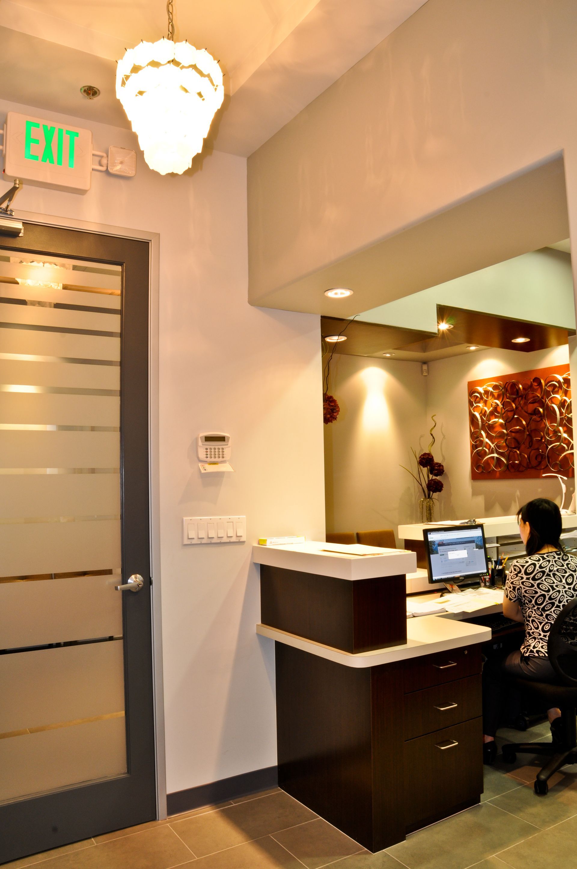 Reception area with person working at desk, door, overhead light, and exit sign.