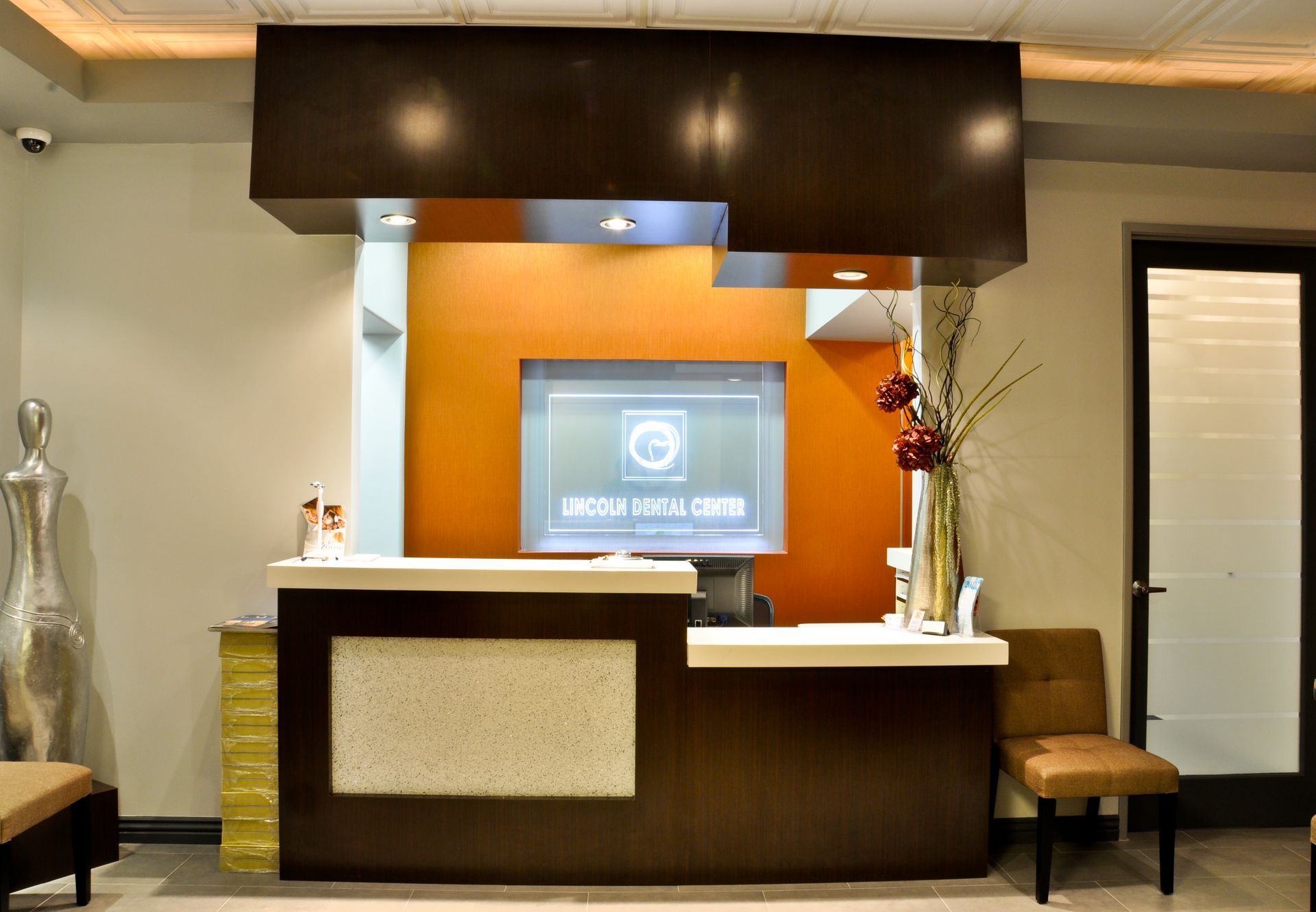 Reception desk in an office, with an orange backdrop, brown desk, and a screen.