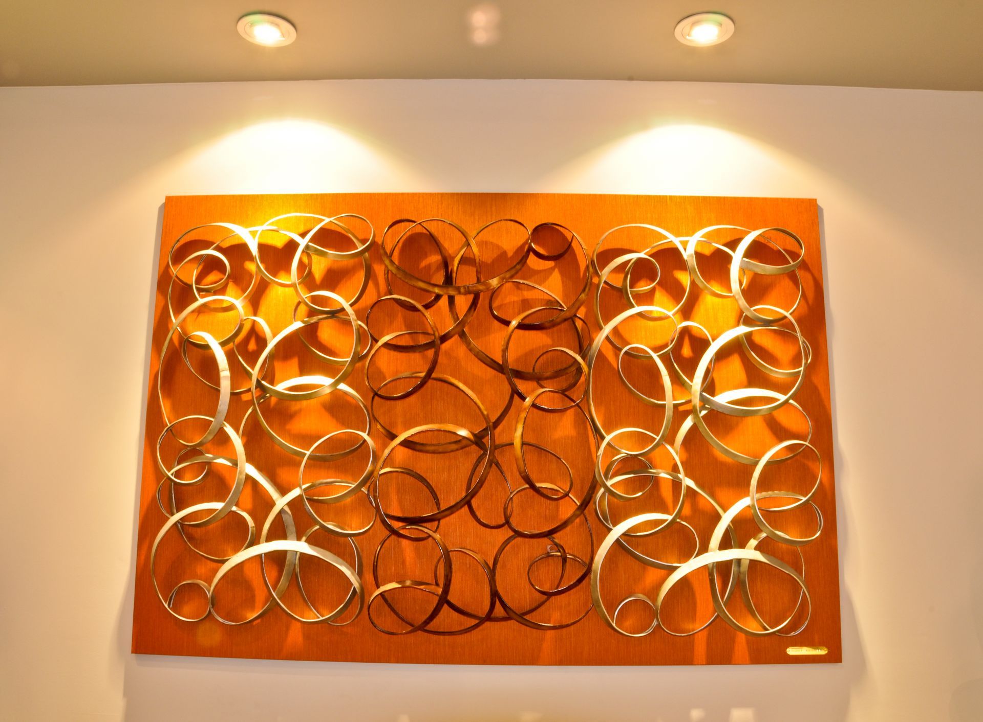 Orange abstract wall art with gold swirling circles, lit by two spotlights.
