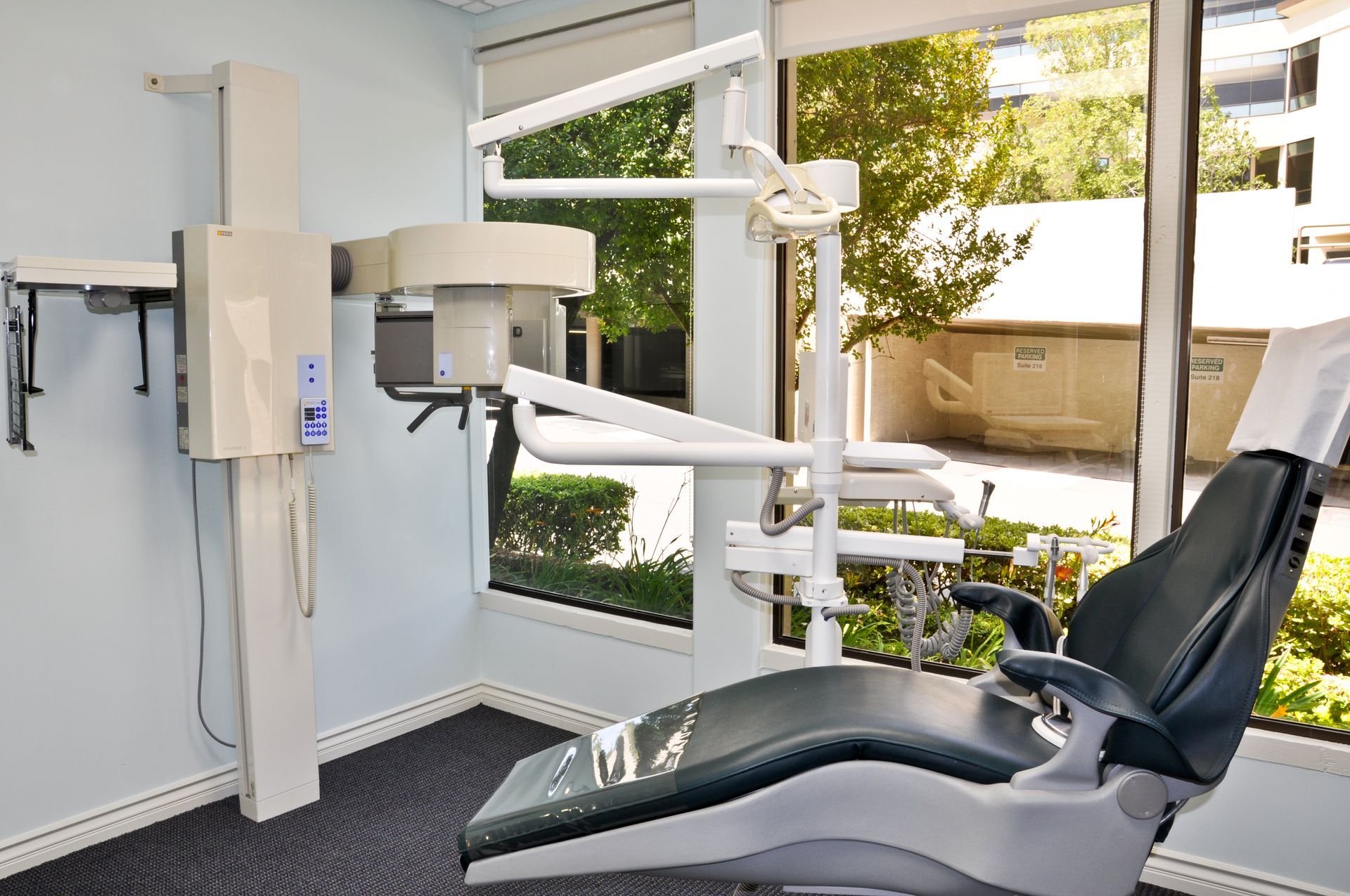Dental office with chair, equipment, and window overlooking greenery.