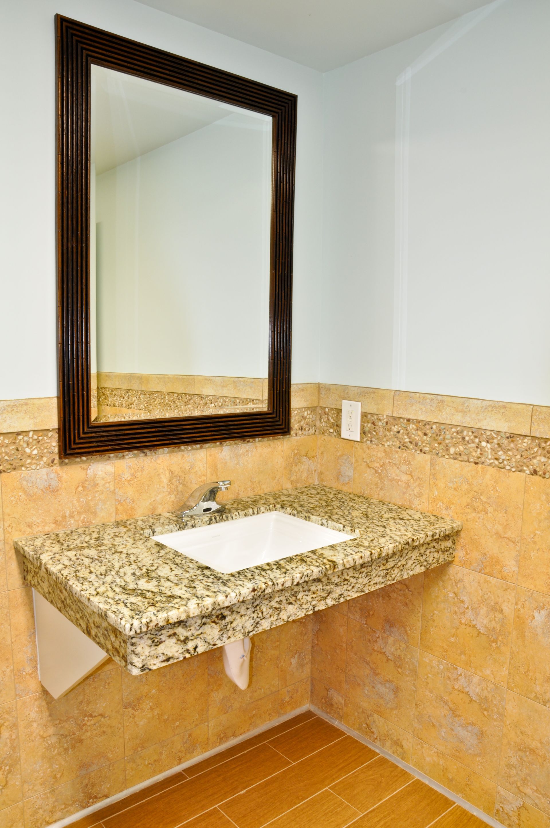Bathroom with granite countertop sink, large mirror, tan tile walls, and wood floor.
