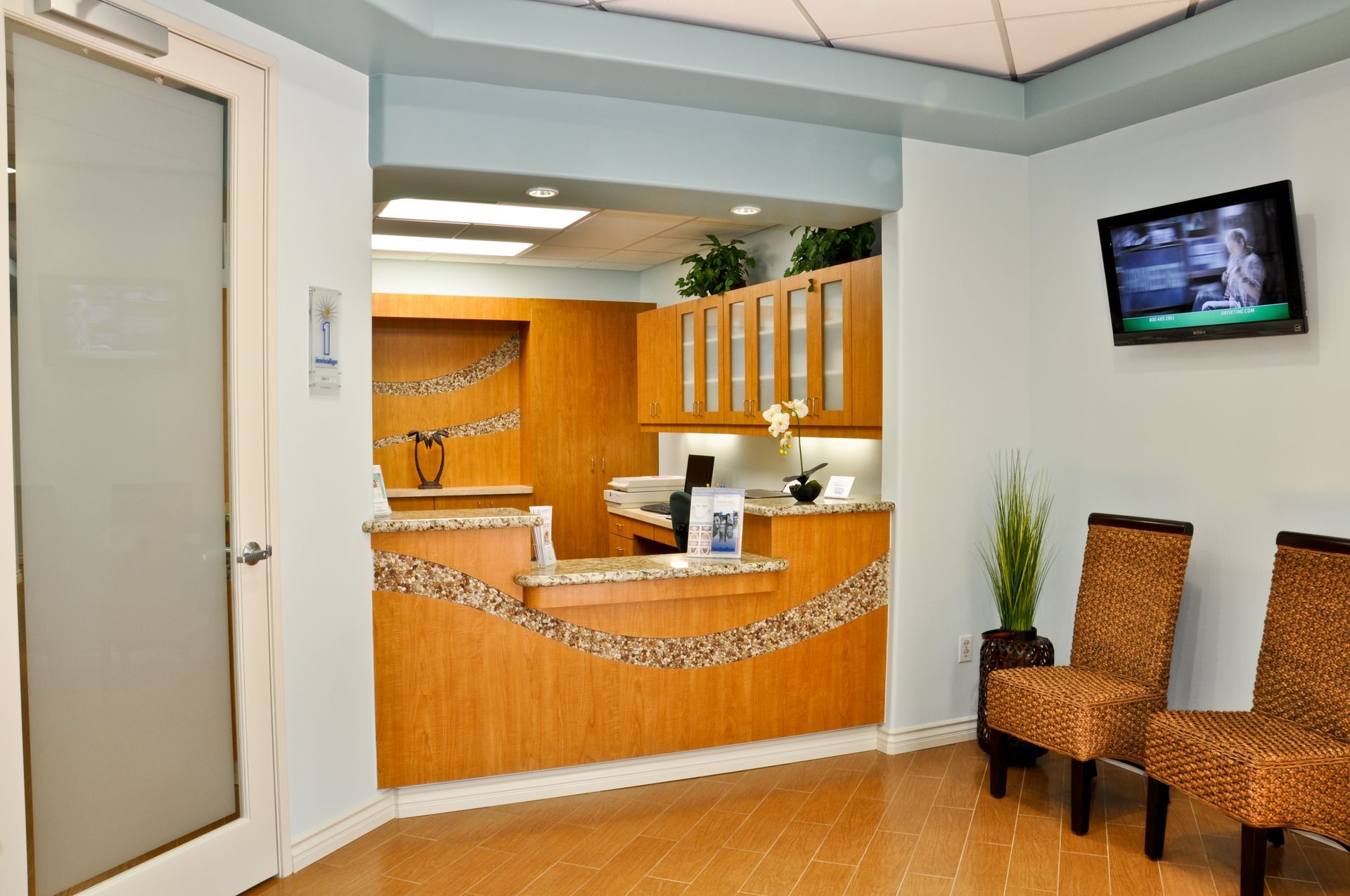 Reception area with light blue walls, wooden reception desk, two chairs, and a TV.