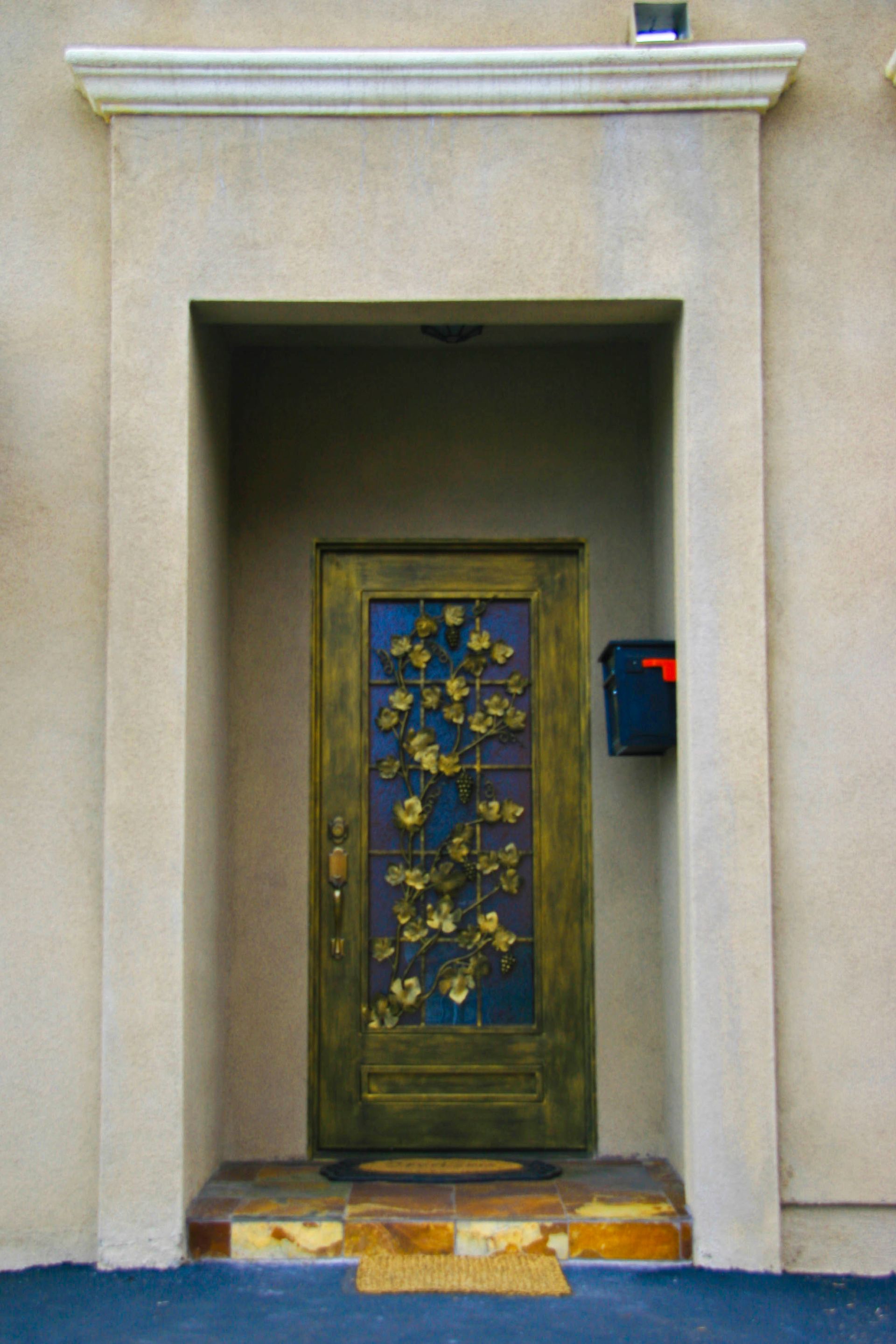 Gold and blue door with flower design in a recessed tan entryway, black mailbox on the right.
