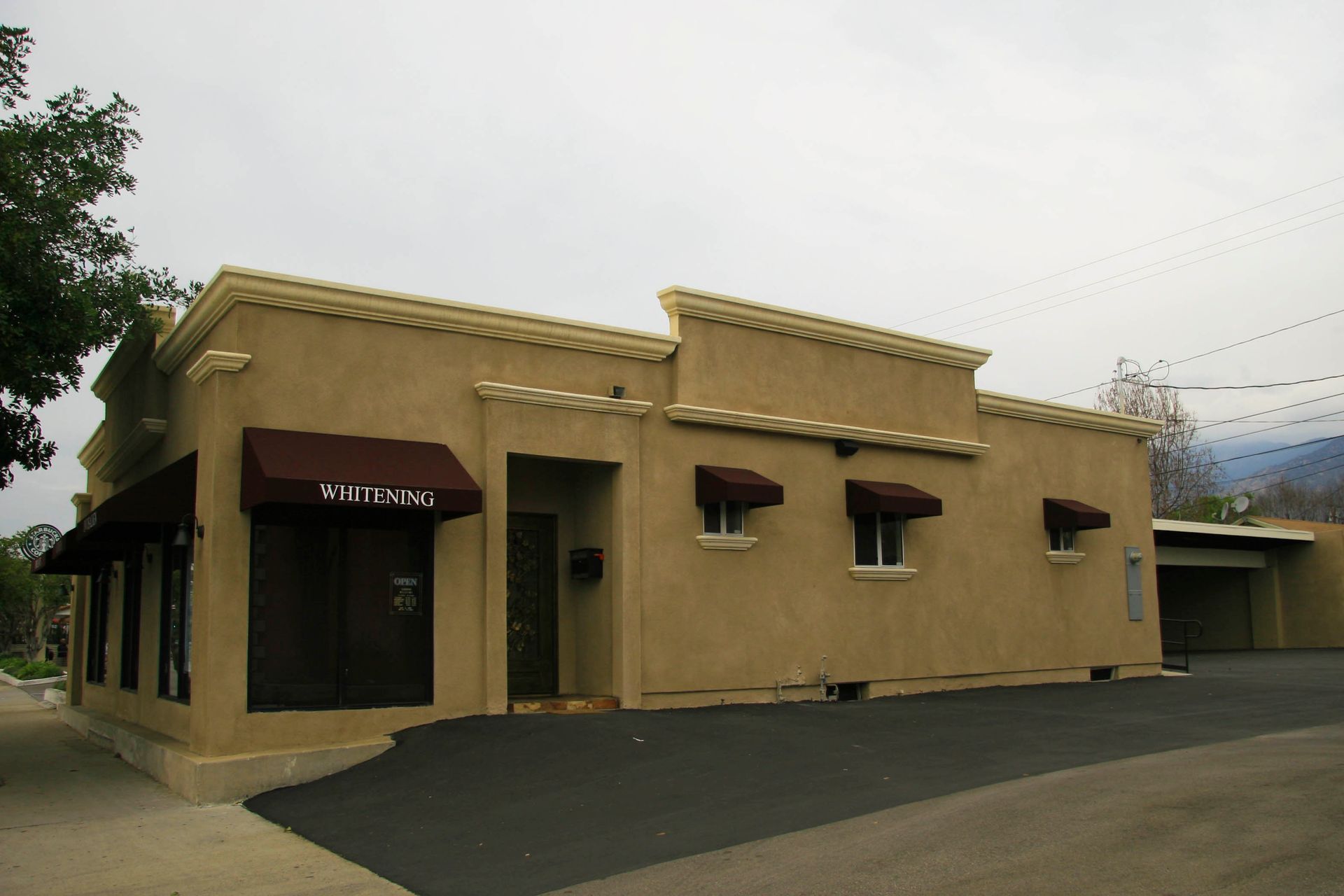 Tan stucco building with brown awnings and trim; asphalt driveway.