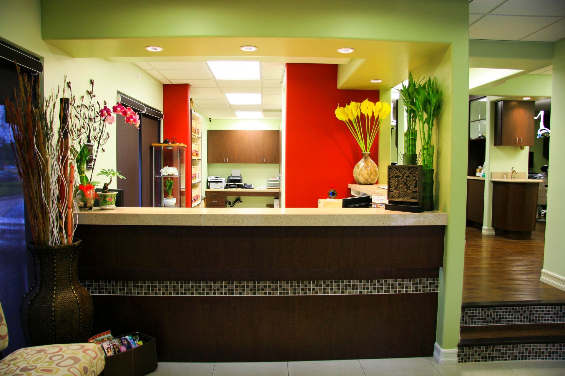 Reception area with a dark brown desk, red wall, and flower arrangements.
