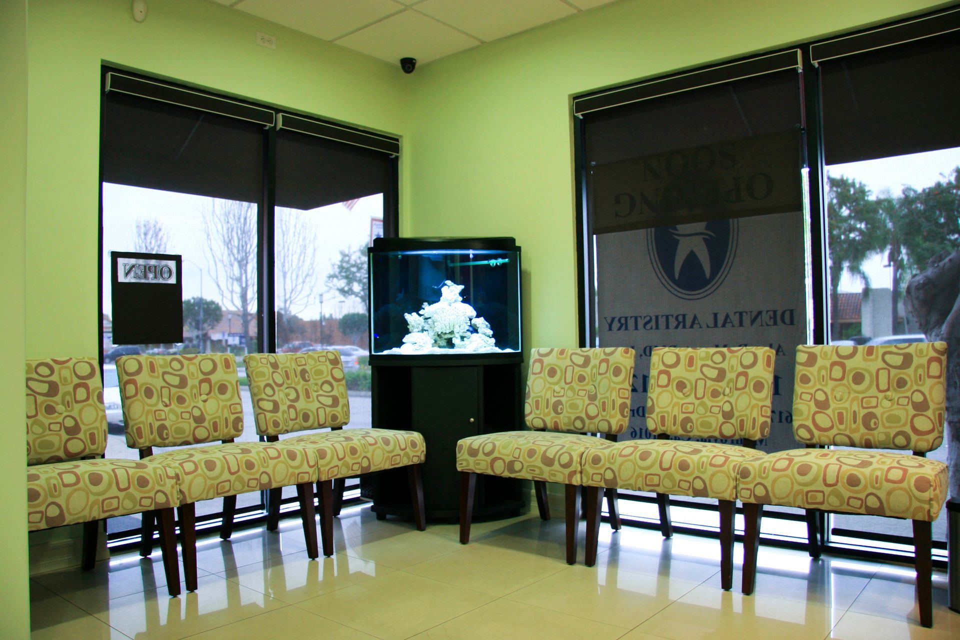 Waiting room with green walls, floral chairs, an aquarium, and large windows.