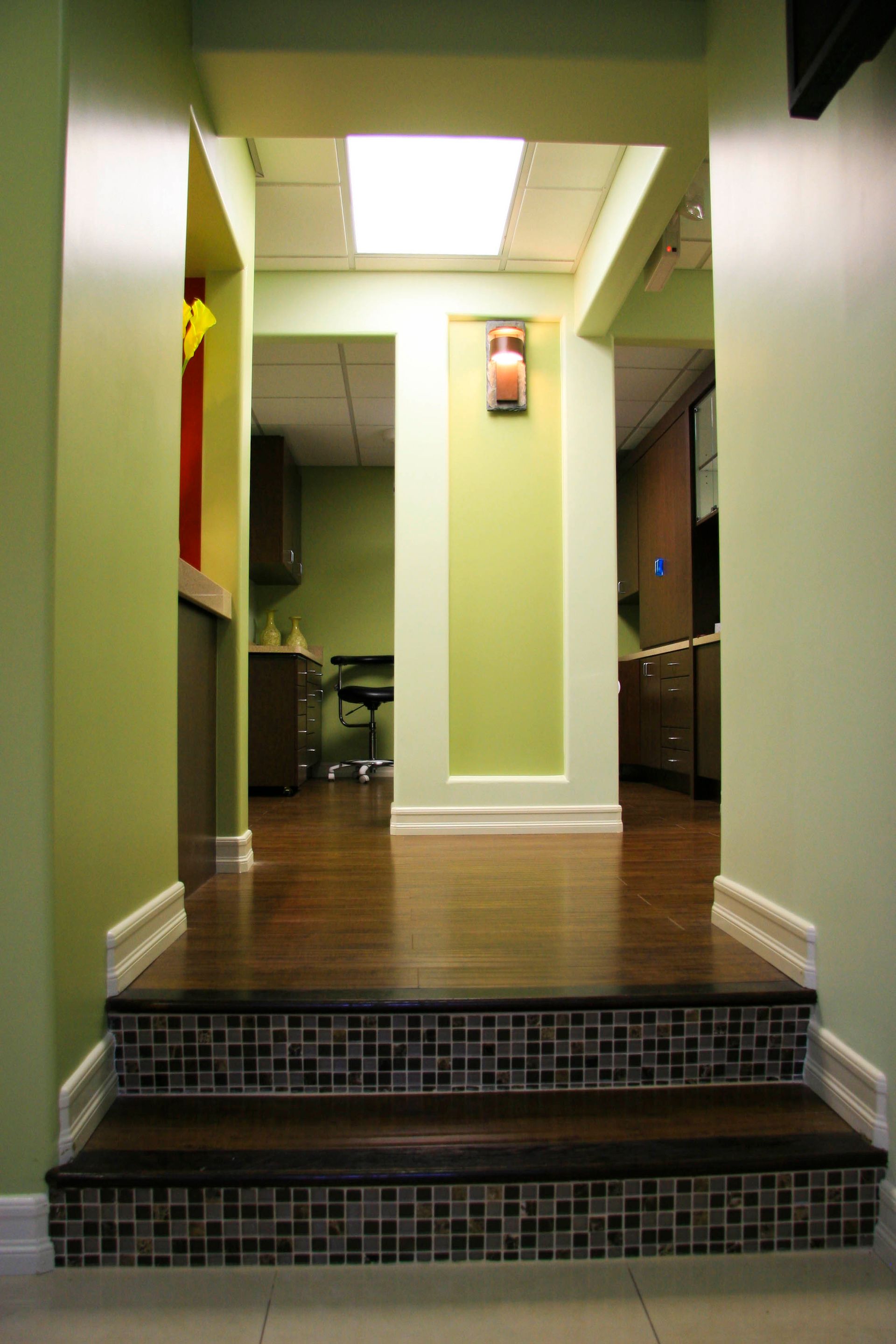 Steps lead to hallway in green-painted dental office, featuring wood floors and decorative tile.