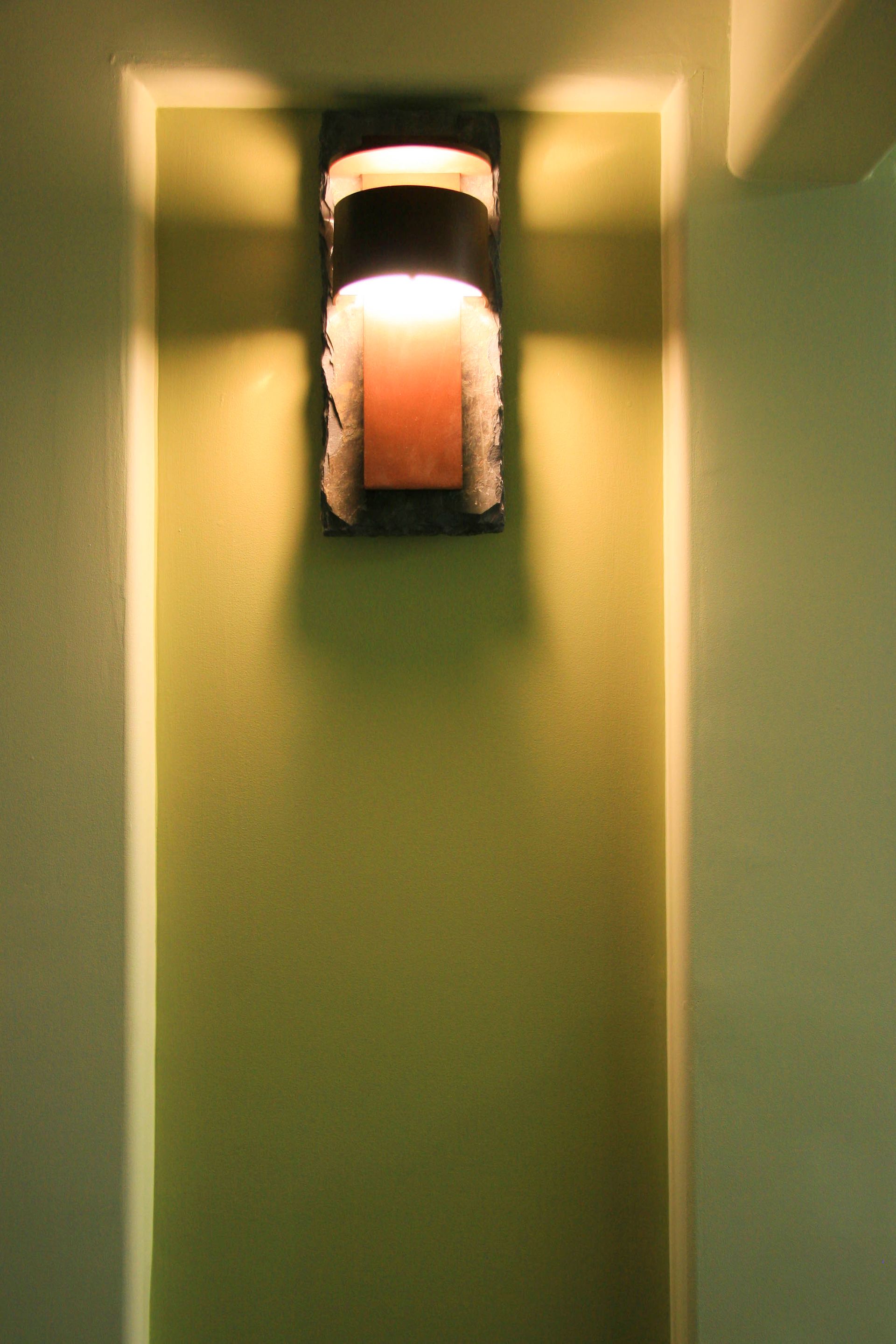 Wall-mounted light fixture in a recessed space, casting a warm glow on green-painted wall.