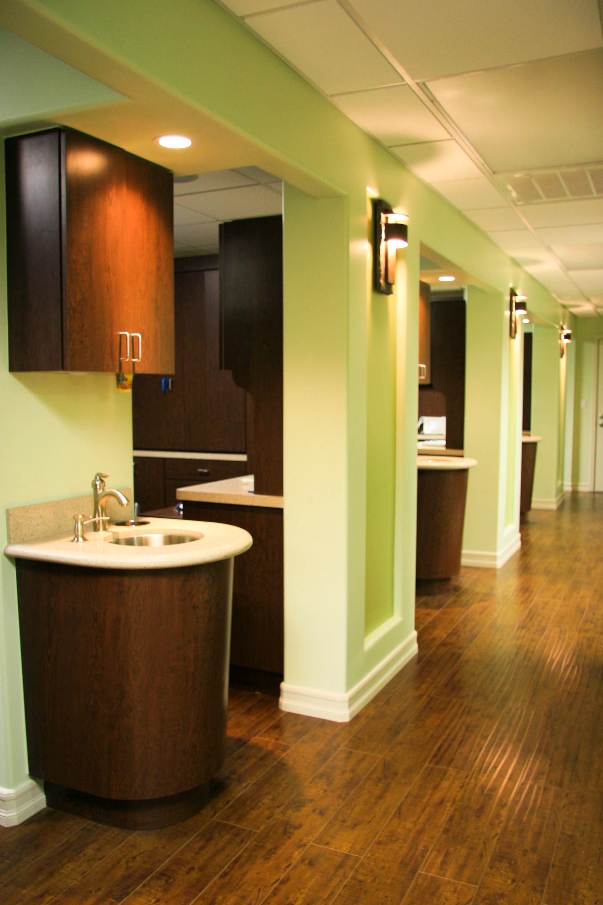A dental office hallway with dark wood cabinets, green walls, and dark wood floor.