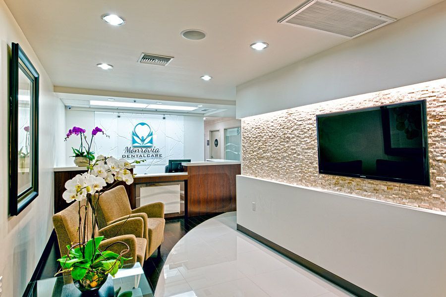 Modern dental office waiting area. Chairs, TV, and reception desk with logo.