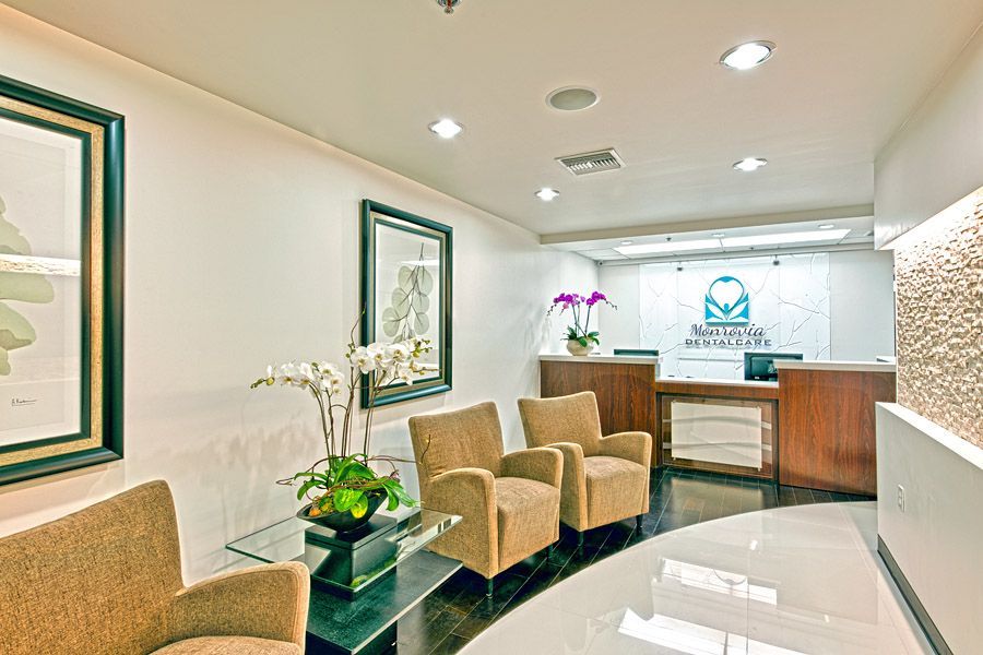 Waiting room with beige chairs, glass table, artwork, and reception desk.