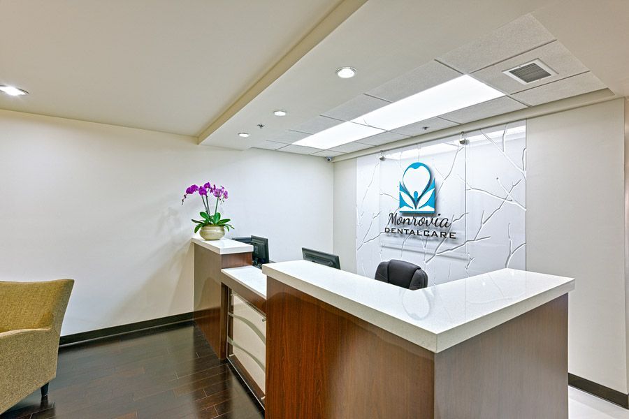 Reception area of a medical office with white walls, dark wood floors, and a logo behind the reception desk.