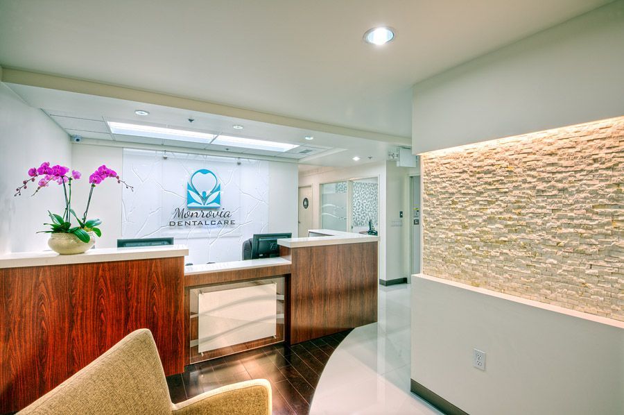 Reception area with desk, logo, and potted orchids; stone accent wall on right.