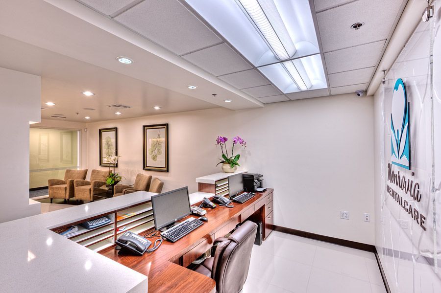 Reception area of a medical office with a wooden desk, computers, and waiting area with chairs.