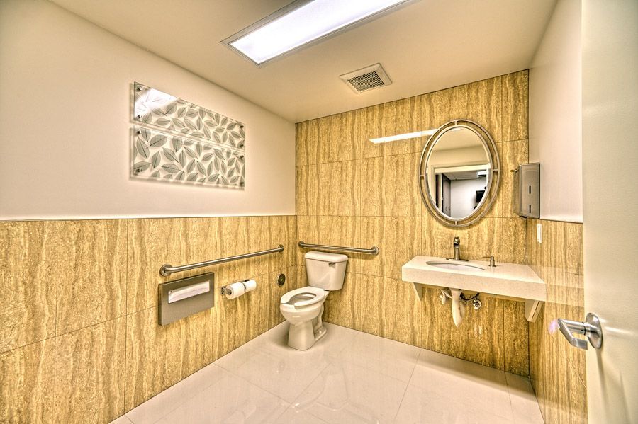 Accessible restroom with beige textured walls, toilet, sink, grab bar, and decorative art.