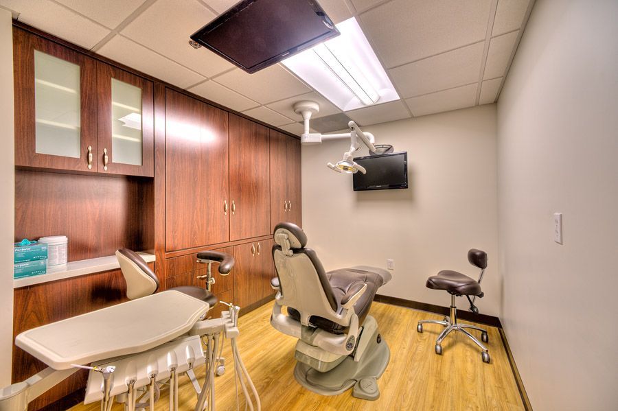 Dental exam room with brown cabinetry, dental chair, equipment, and mounted TV.