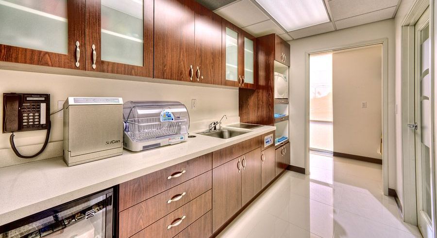 A dental office sterilization room with cabinets, sink, and equipment; wood and white tones.