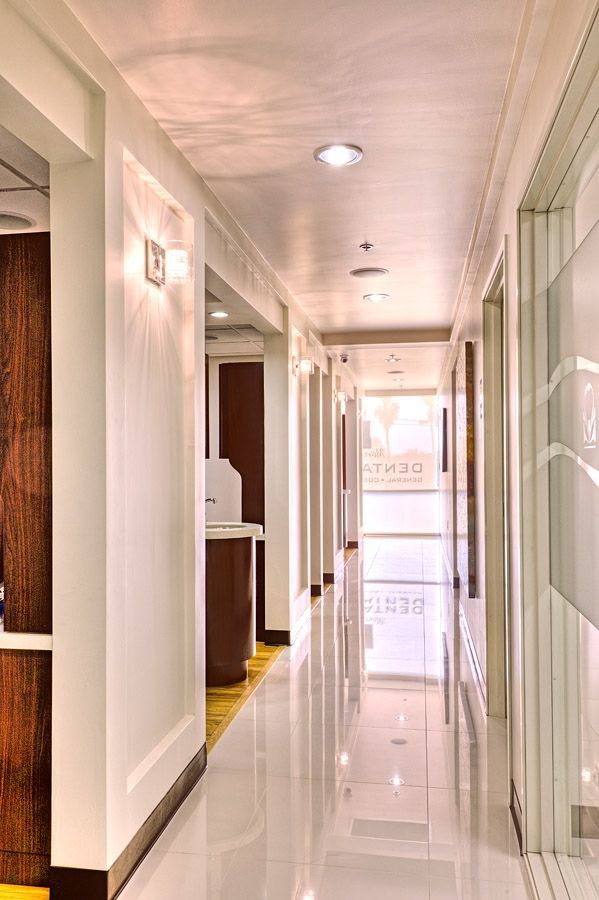 Narrow, well-lit hallway in a clinic with white walls, glossy floors, and doors.