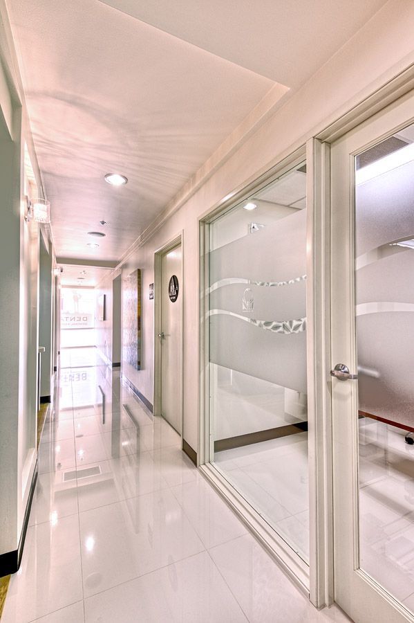 White hallway with doors on both sides, a window with frosted design, and bright lighting.
