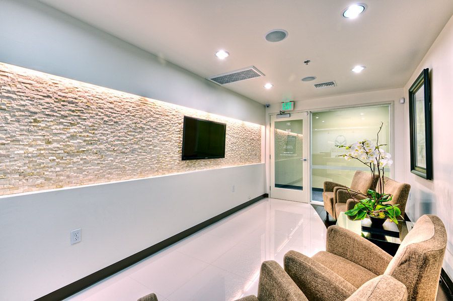 Modern waiting room with beige stone wall, TV, and tan chairs.