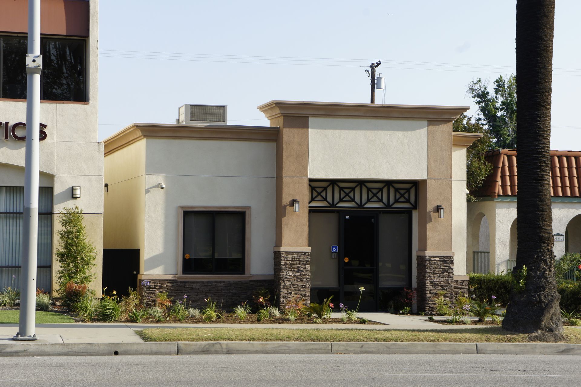 A small tan building with a brown trim and entrance.  Stone accents at the bottom. Landscaped yard in front.