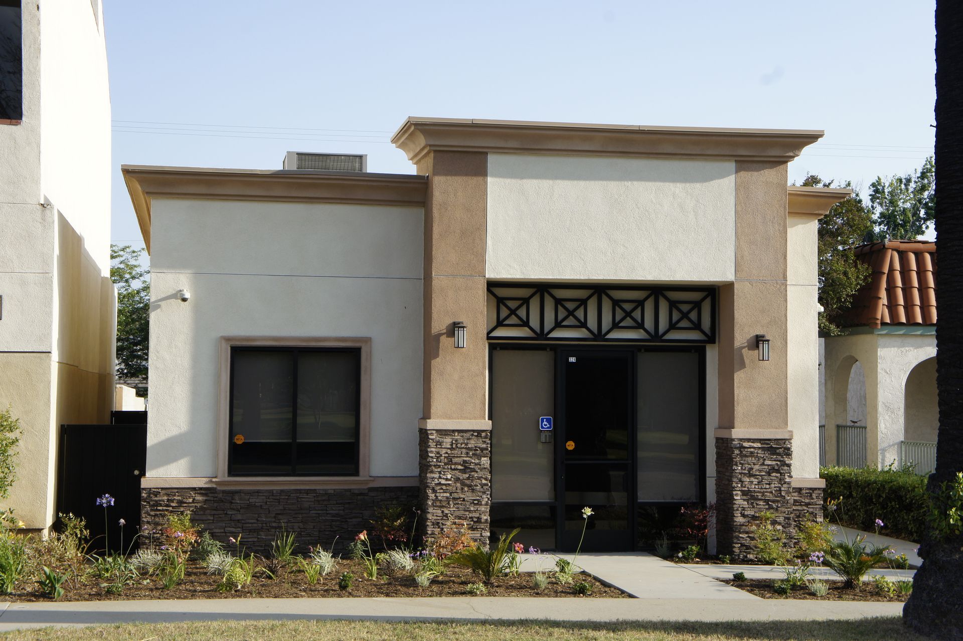 Small commercial building with tan, cream, and brown exterior. Features window, door, and landscaping.