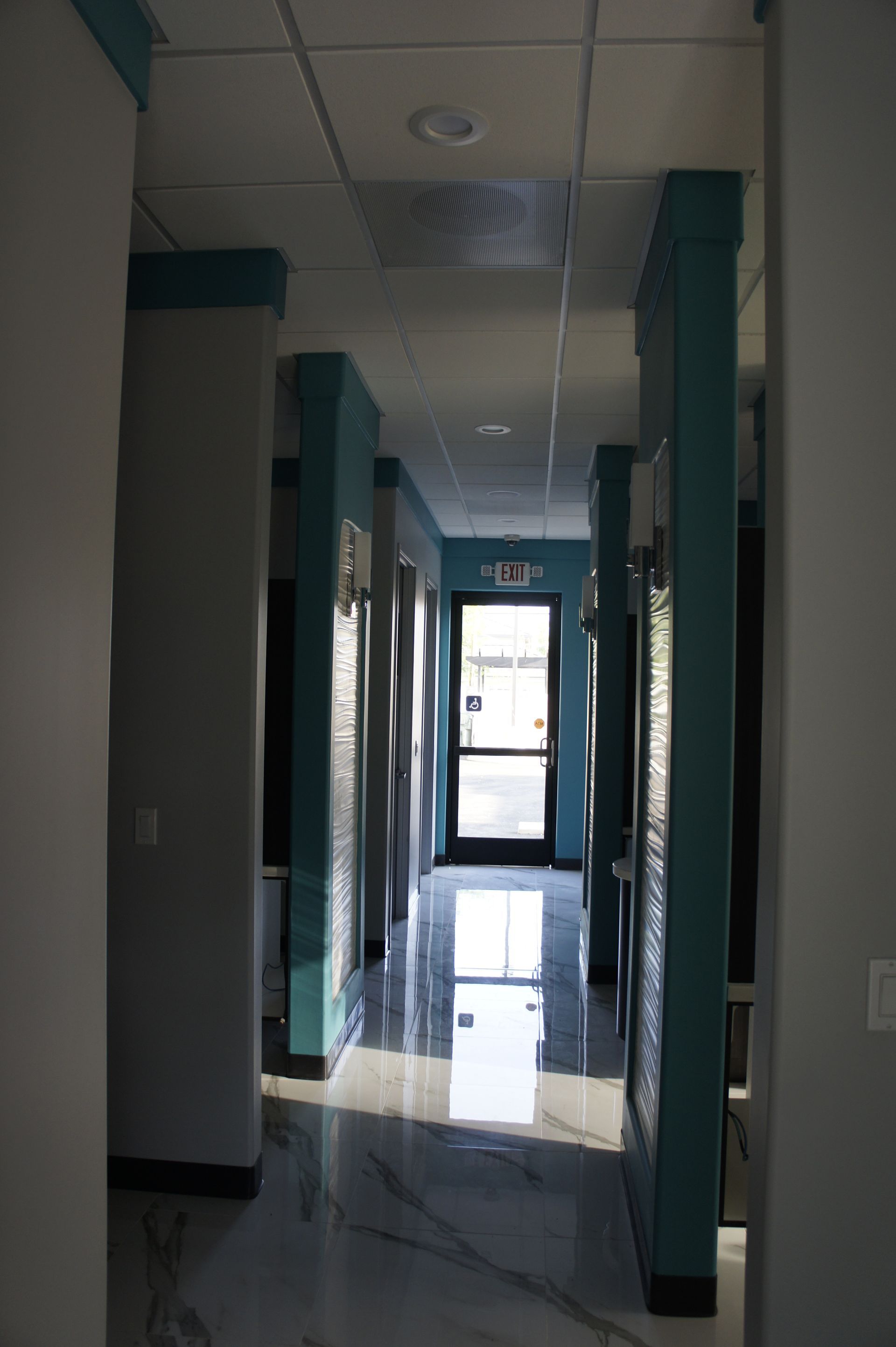 Hallway with glossy floor, teal accents, gray walls, and door at the end.
