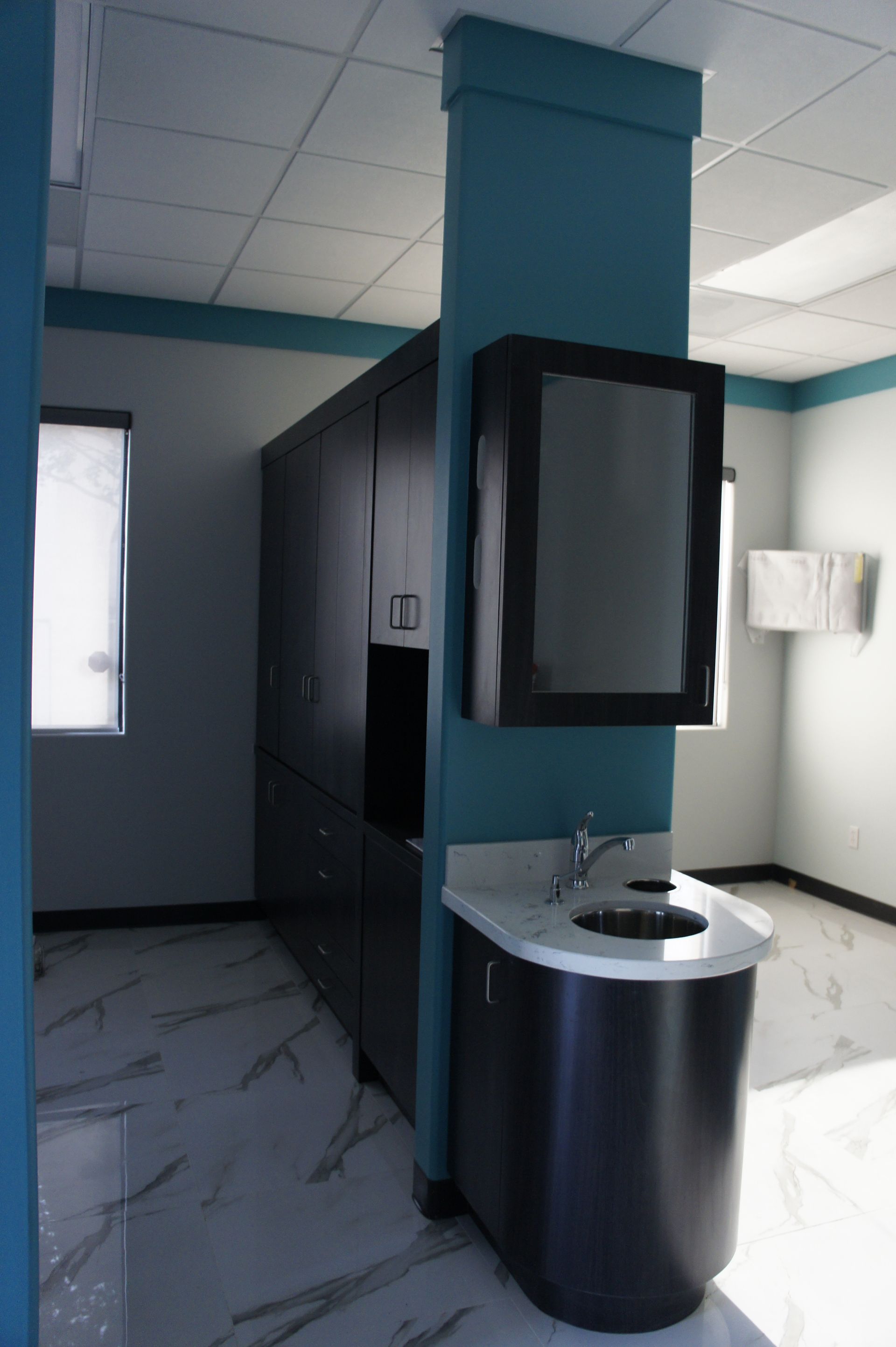 Dental office with dark cabinetry, a sink, a mirror, and teal accents.