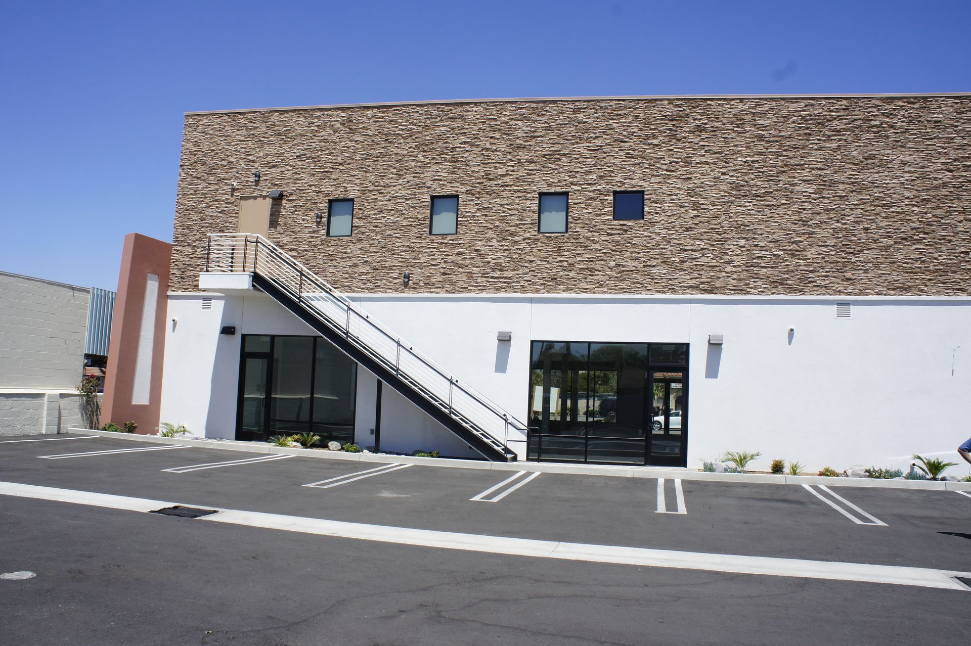 Building with stone upper level, white lower level, metal fire escape, and parking spaces.