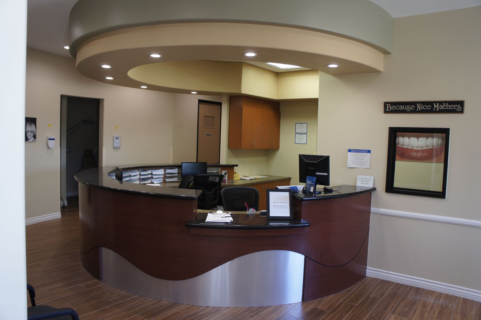 Reception desk in a dental office, dark wood and stainless steel accents, beige walls and floors.