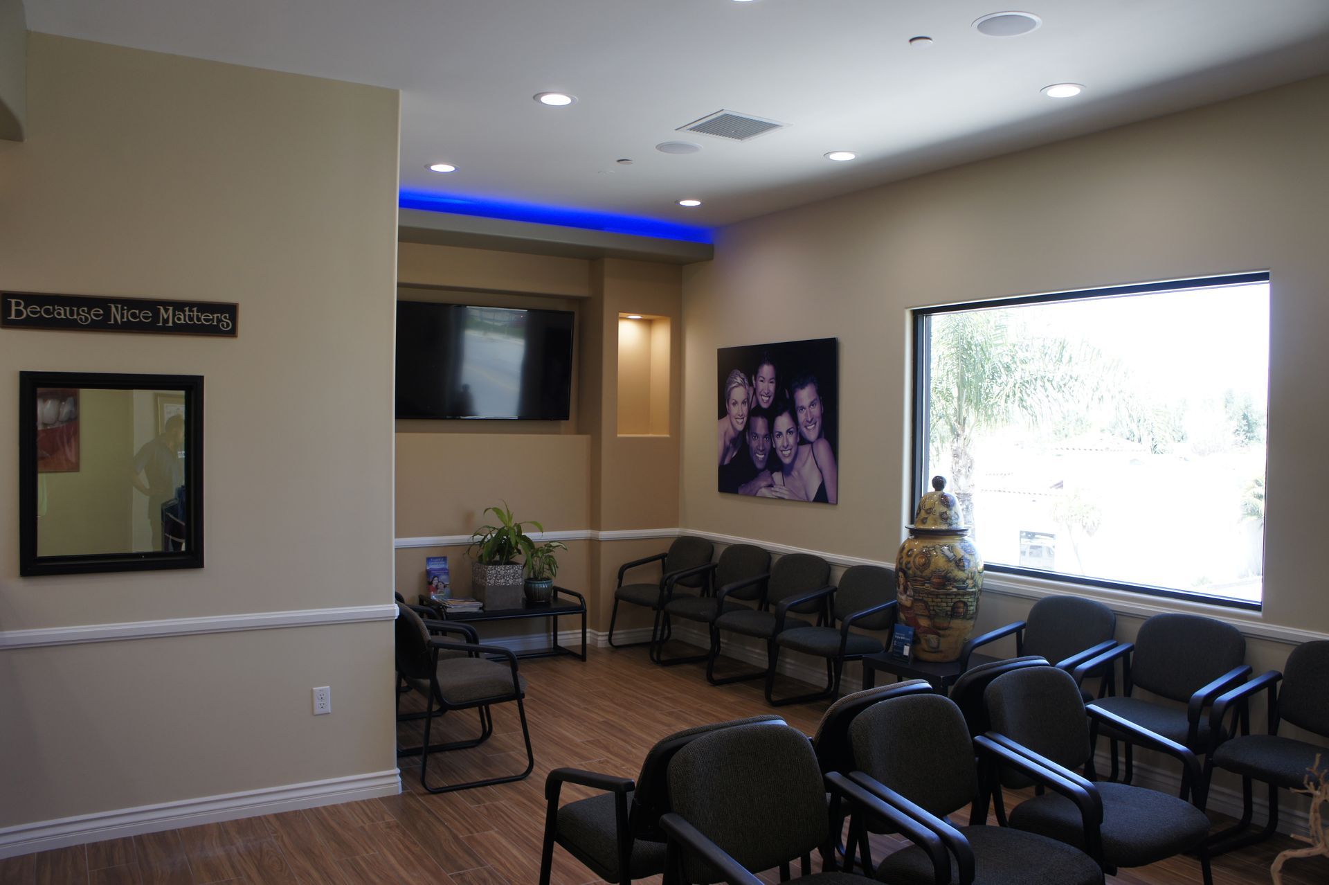 Waiting room with chairs, TV, family portrait, and window. Beige walls with blue accent lighting.