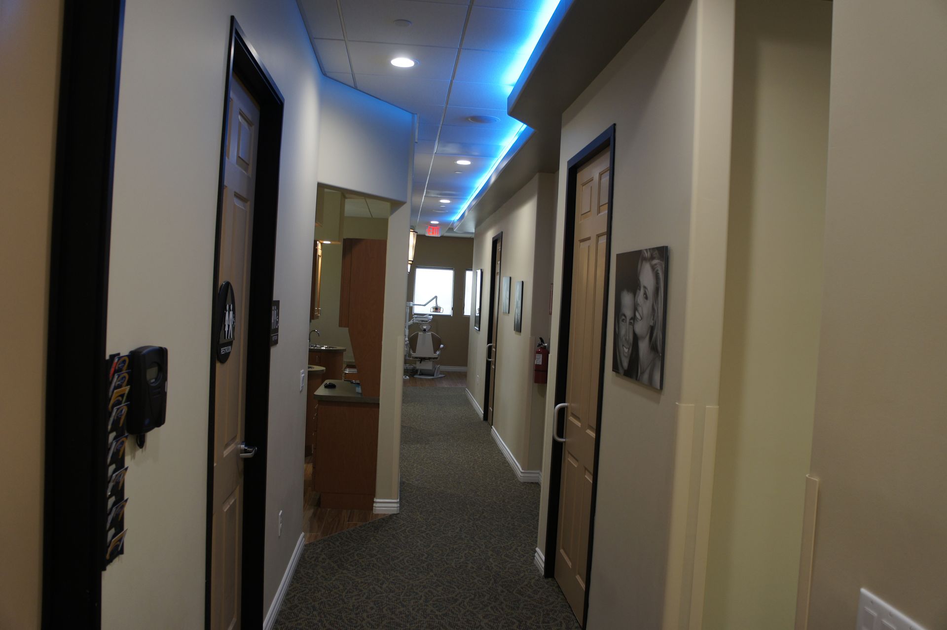 Hallway in an office, with closed doors, carpet, and blue ceiling lighting.