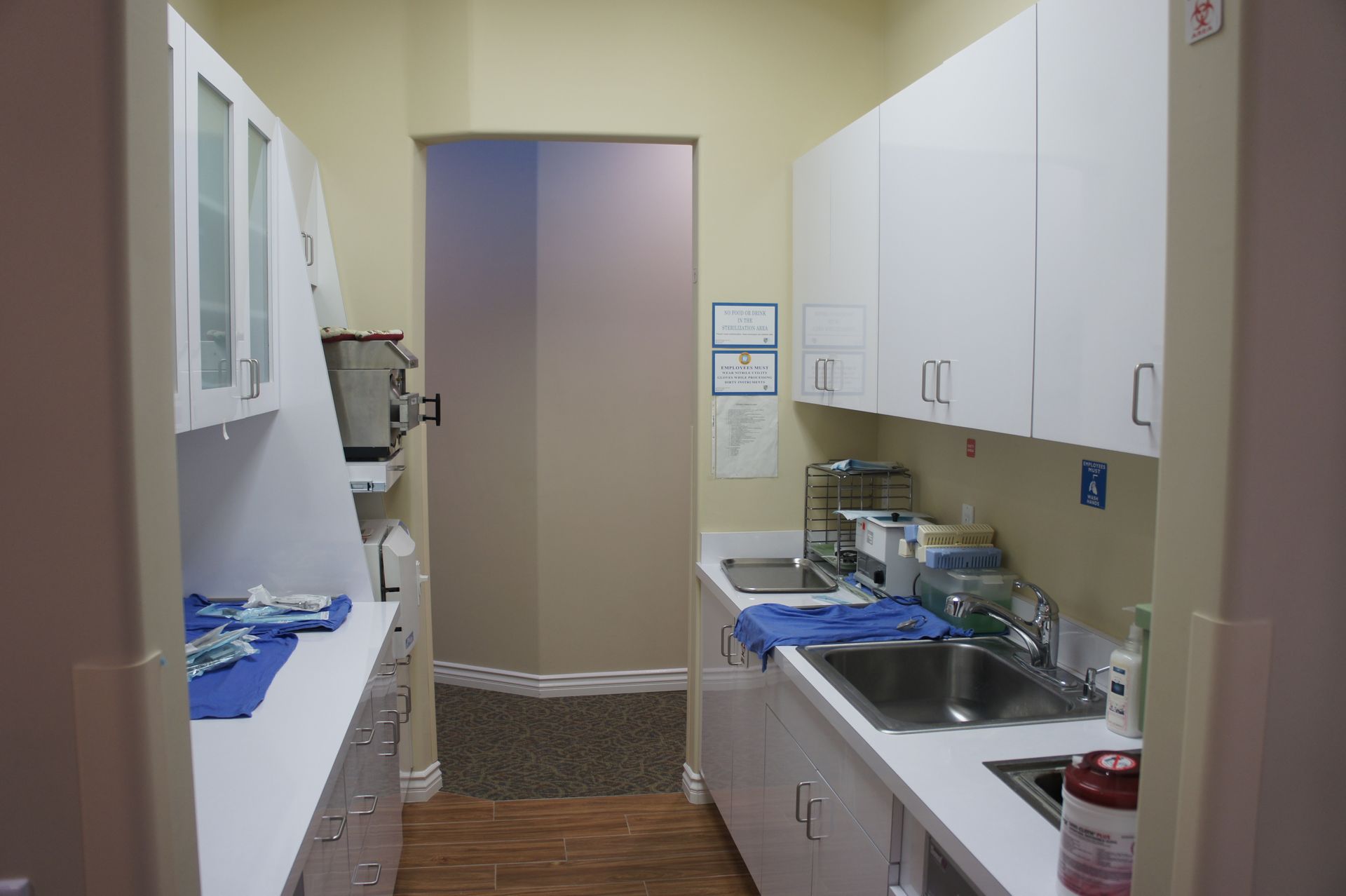 Dental office sterilization room with white cabinets, stainless steel sink, and a closed doorway.