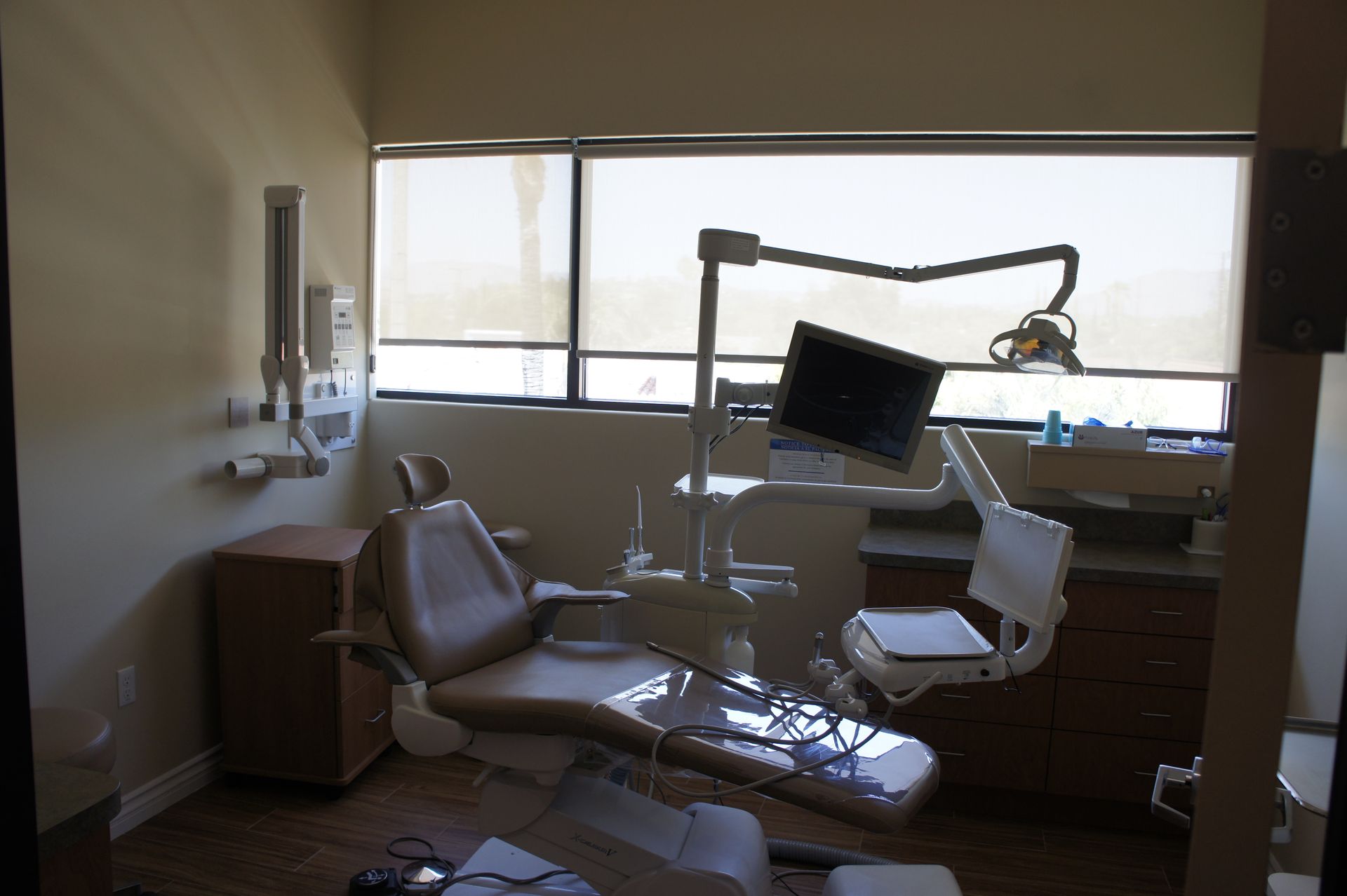 Dental office with beige chair, light, monitor, and window with blinds.