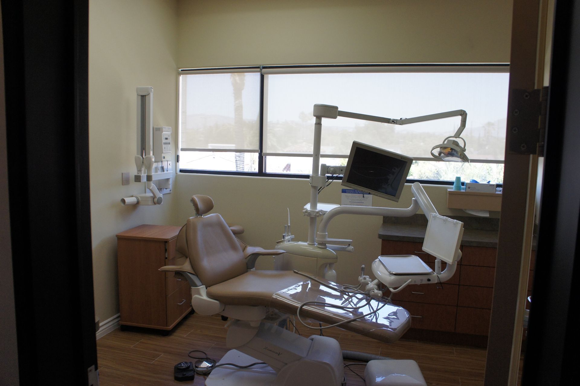 Dental office with tan dental chair, equipment, and window.