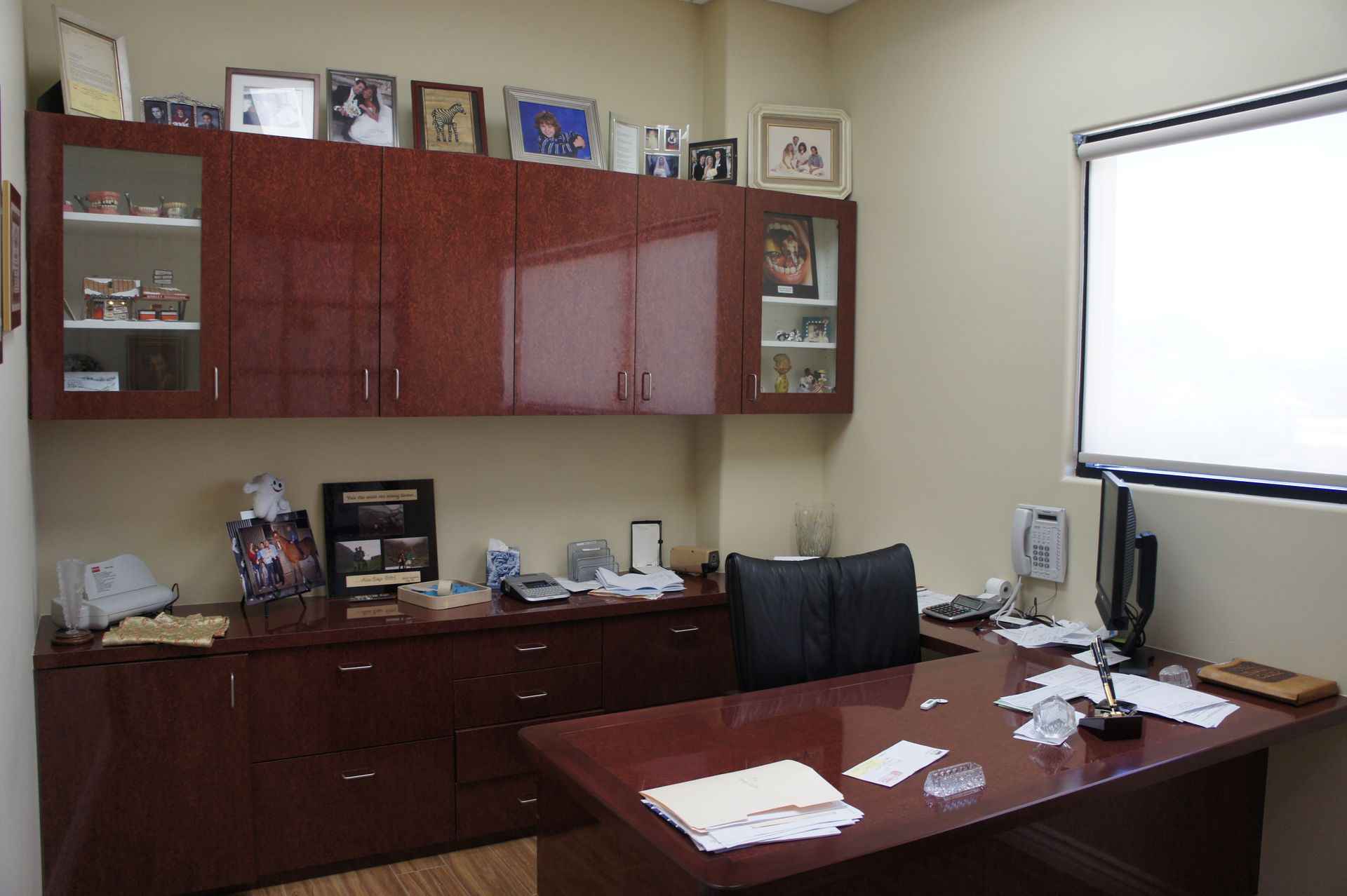 Office with dark wood desk and cabinets, items on desk and shelves, neutral walls, and a window.