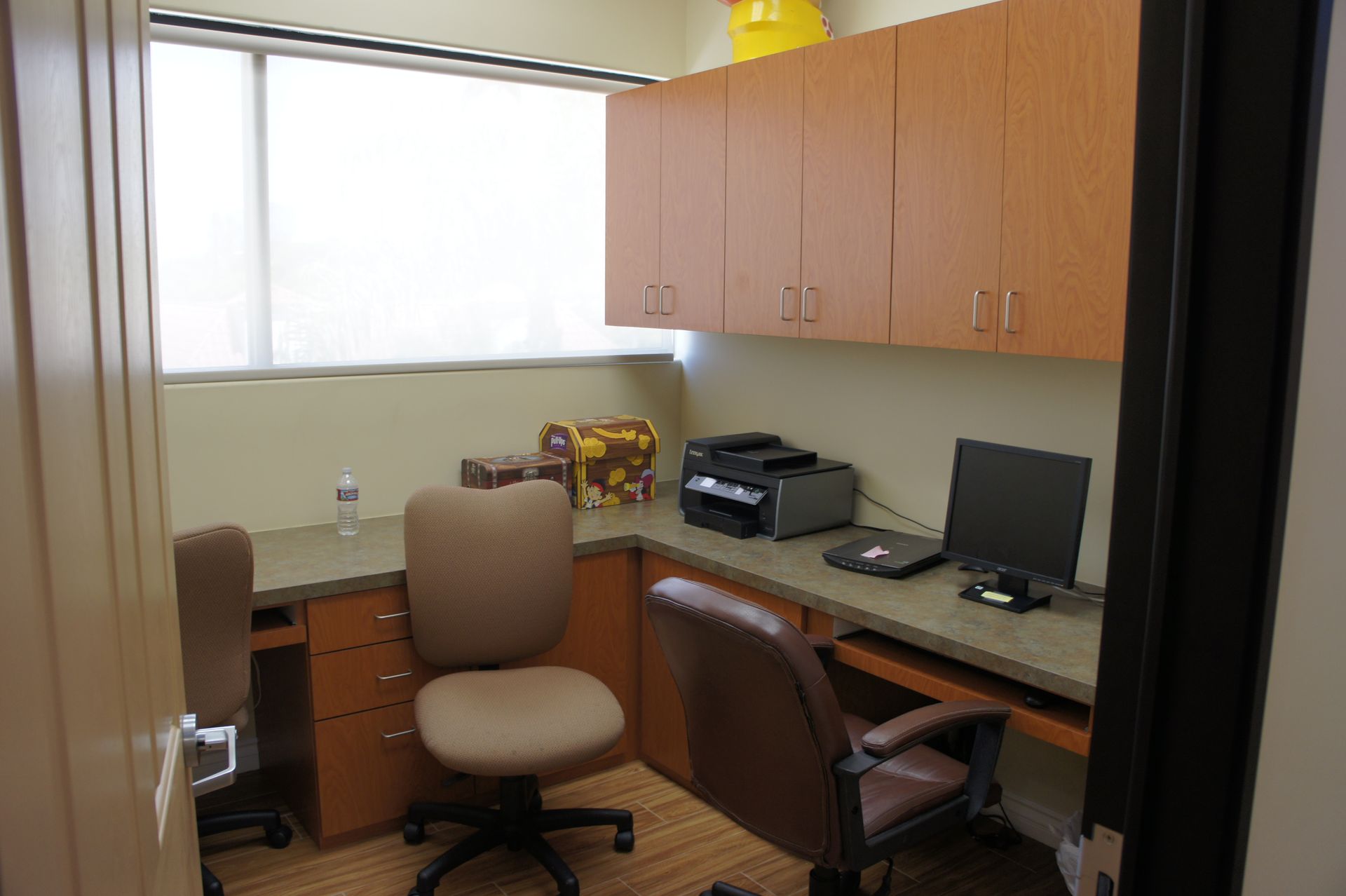 Small office with desks, cabinets, window, chairs, and computer.