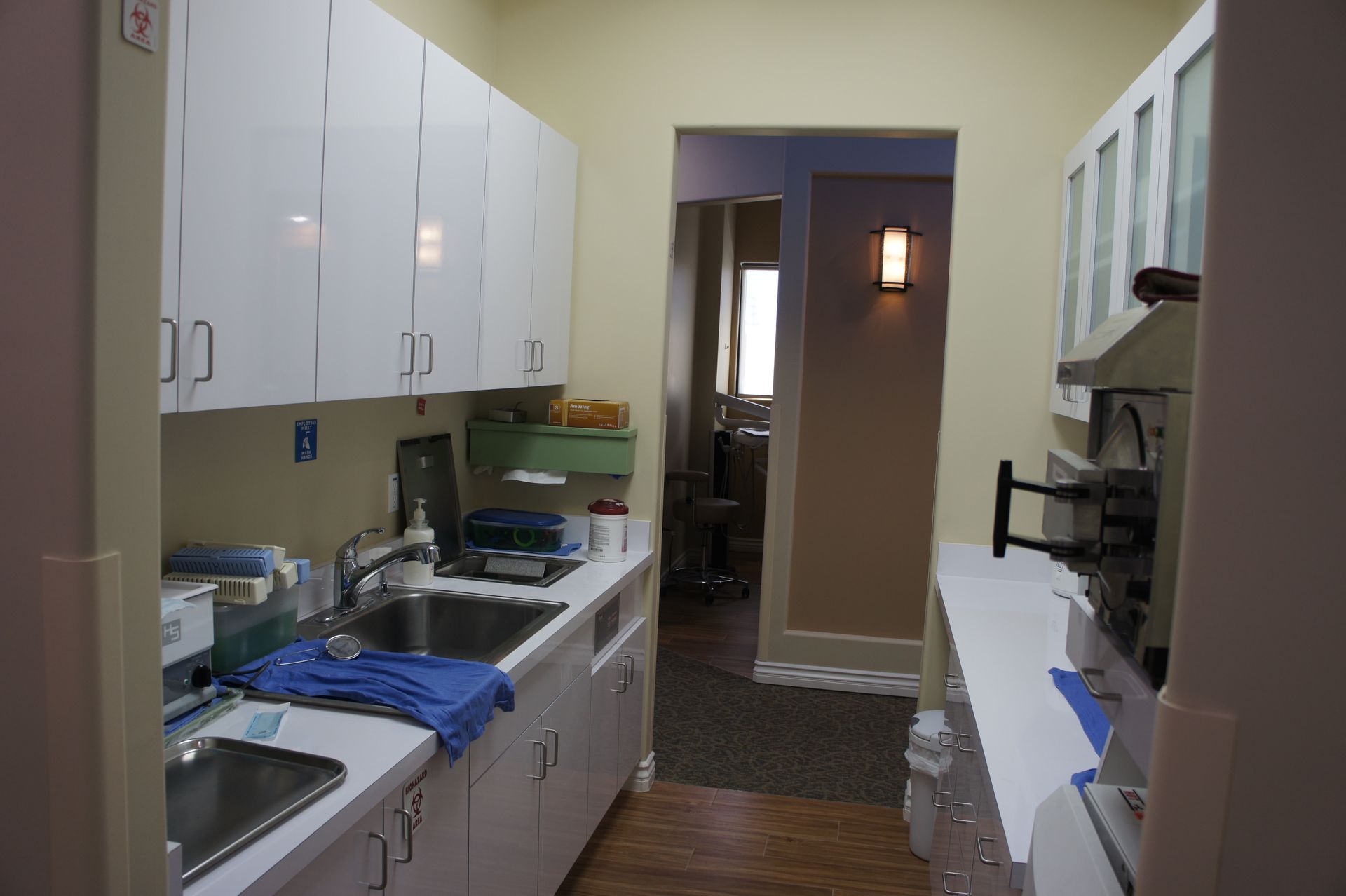 A dental office utility room with white cabinets, sink, and a doorway to another room.