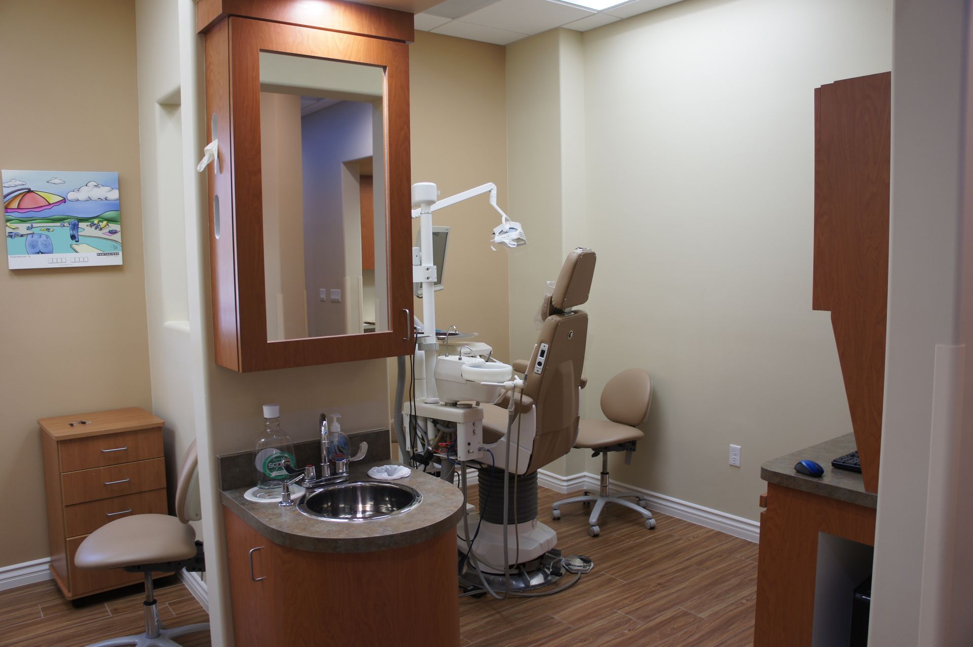 Dental exam room with chair, sink, cabinetry, and light beige walls.