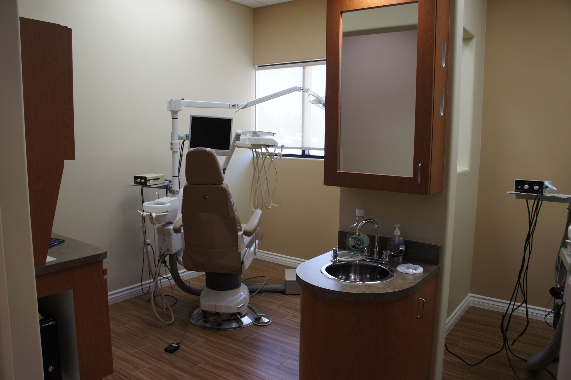 Dental exam room with beige walls, brown dental chair, and sink.